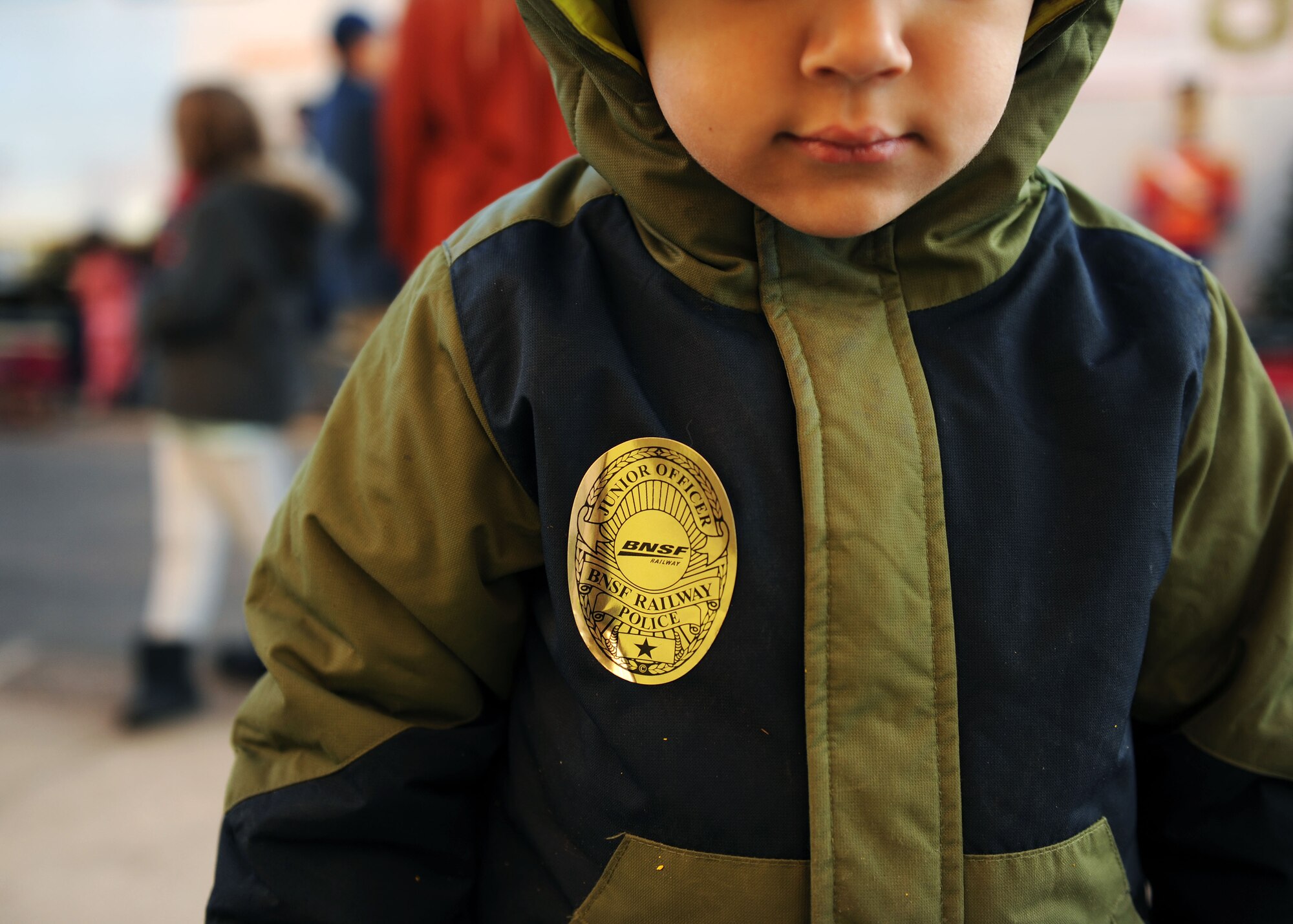 A dependent from Cannon Air Force Base, N.M., waits to board the Holiday Express wearing a novelty BNSF Railway Junior Officer badge, Dec. 1, 2016, at a railyard in downtown Clovis, N.M. For nine consecutive years, the BNSF Railway has invited service members and their loved ones aboard the Holiday Express to enjoy milk, cookies, and a visit from Santa Claus to show their appreciation. (U.S. Air Force photo by Staff Sgt. Whitney Amstutz/Released)  