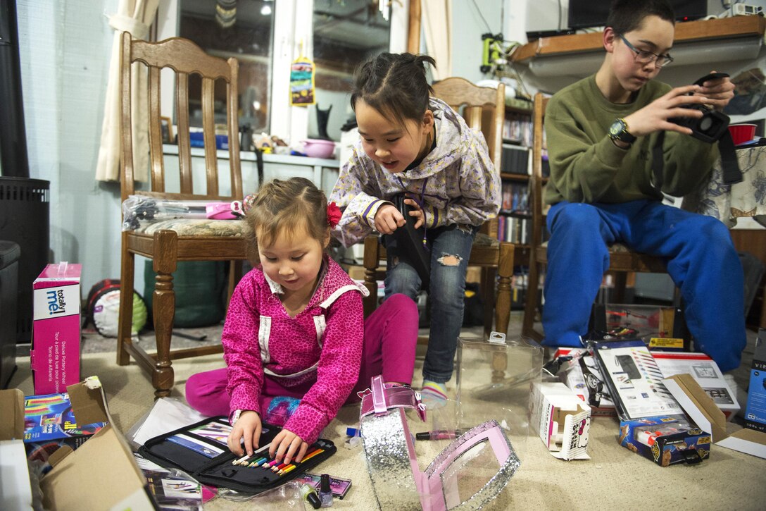 From left to right: Shanelle, 6, Audrey, 11, and Martin, 13, open their Christmas presents during Toys for Tots at Sikusuiliaq Hatchery, Alaska, Dec. 4, 2016. Air Force photo by Alejandro Pena
