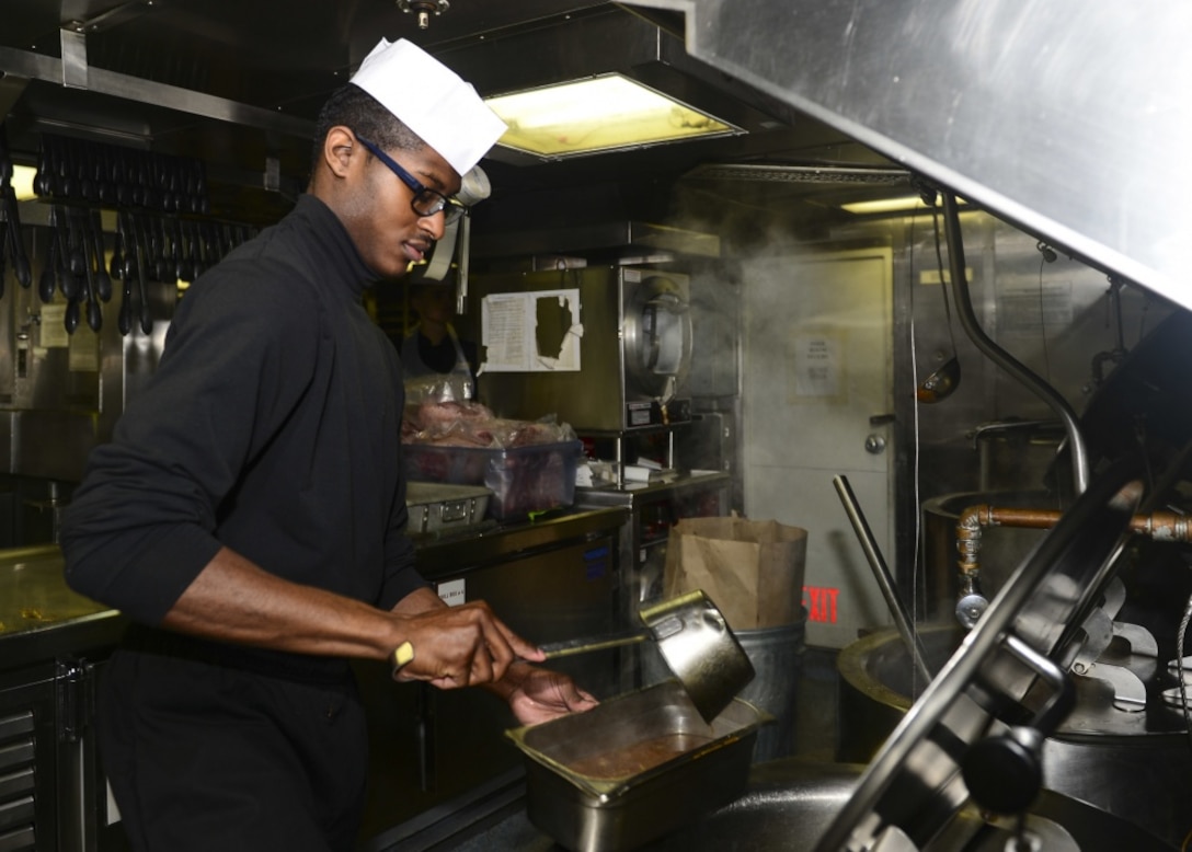 Navy Seaman Travis McCalman ladles baked beans into a serving tray in the galley aboard the amphibious dock landing ship USS Whidbey Island, Oct. 26, 2016. Navy photo by Petty Officer 2nd Class Nathan R. McDonald