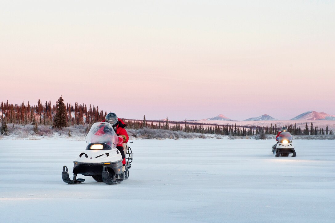 Marine Corps 1st Sgt. Joshua Guffey, foreground, and Capt. Michael Sickels ride their snow machines over a frozen Alaskan lake as they return to their unit after participating in Toys for Tots, Dec. 5, 2016.  Air Force photo by Alejandro Pena