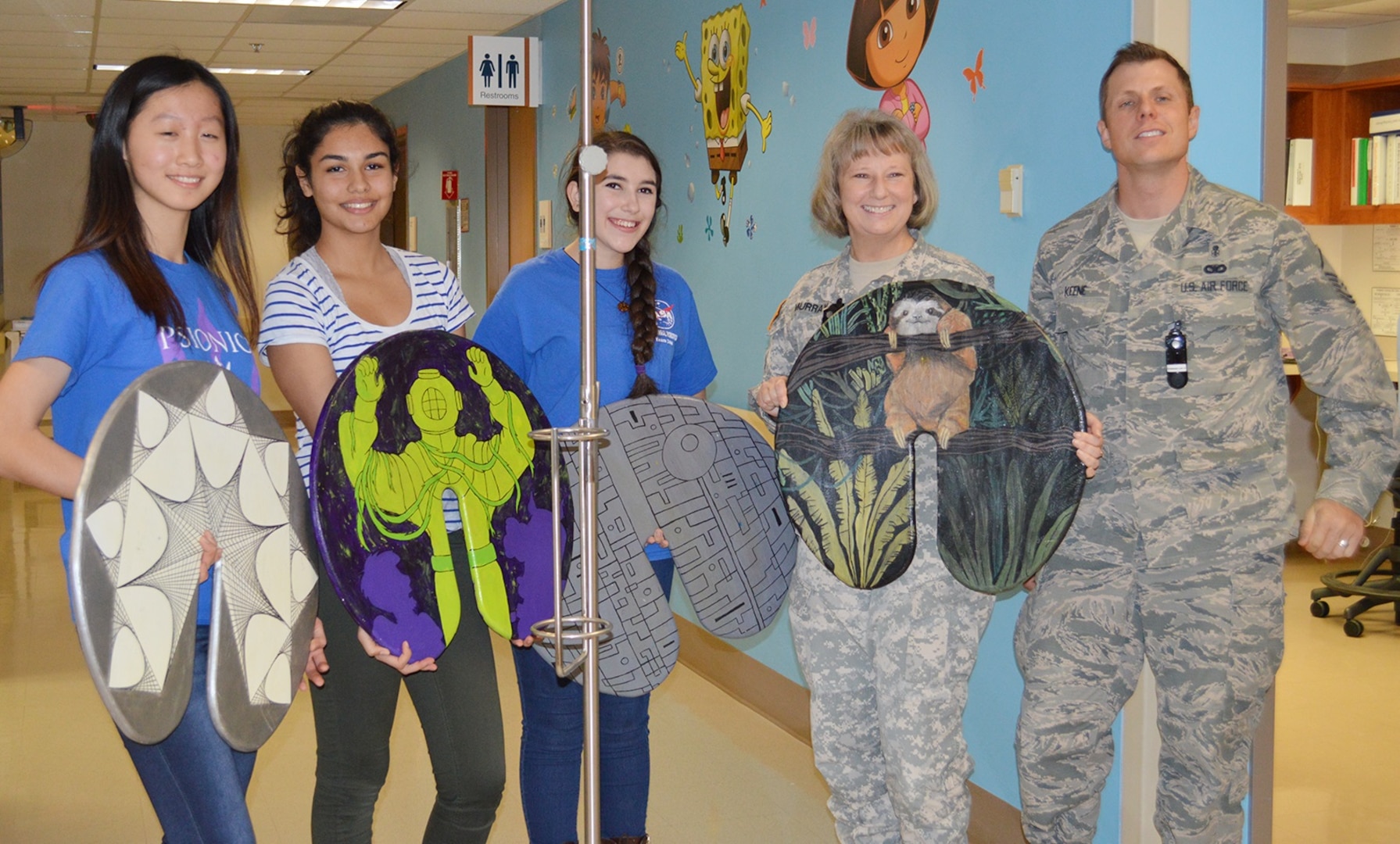 (From left) Lillian Sun, Amaya Mali and Sophie Rosenberg, students with the Westlake Robotics Club, display a few of their donated IV pole “lily pads” with the help of Army Col. Elizabeth Murray and Air Force Master Sgt. Sean Keene in an inpatient pediatric ward. The Robotics Club students constructed and donated 10 lily pads to pediatric patients at Brooke Army Medical Center at Joint Base San Antonio-Fort Sam Houston Dec. 1.