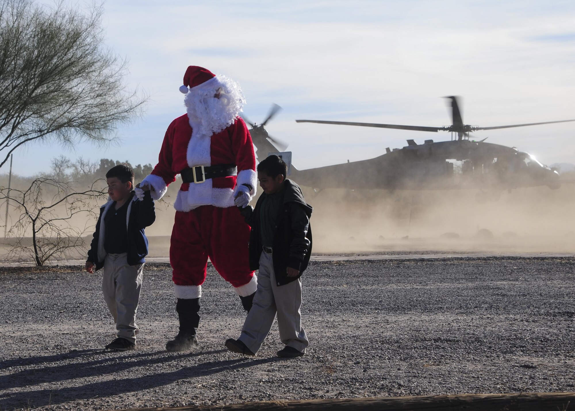 Santa Claus holds hands with students after landing in an HH-60G Pave Hawk during the Santa’s in Blue event at San Xavier Mission School in Tucson, Ariz., Dec. 13, 2016. This year, Santa delivered gifts donated by D-M Airmen to more than 1,000 students at four different schools in the Tucson area. (U.S. Air Force photo by Airman Nathan H. Barbour)