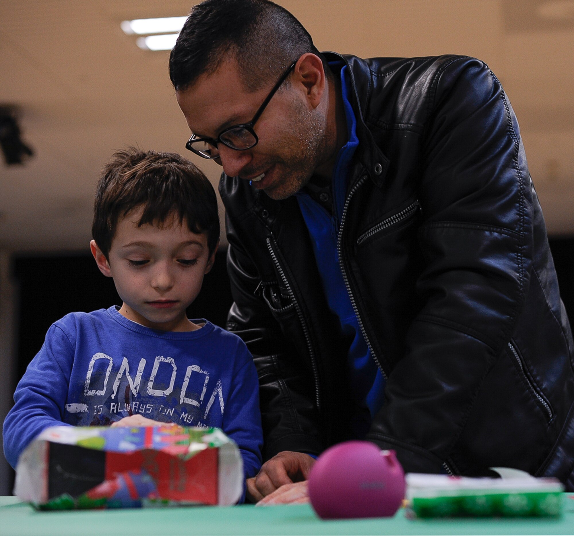Kaan Illanez-Fetah and his father, retired Maj. Jhames Illanez, wrap a gift at Elf Bootcamp at Ramstein Air Base, Germany. Elf Bootcamp is an annual holiday celebration for young children to participate in elf-themed activities such as wrapping gifts. This year’s Elf Bootcamp was free for children under 3 years old and for families of deployed service members. (U.S. Air Force photo by Airman 1st Class Savannah L. Waters)