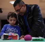 Kaan Illanez-Fetah and his father, retired Maj. Jhames Illanez, wrap a gift at Elf Bootcamp at Ramstein Air Base, Germany. Elf Bootcamp is an annual holiday celebration for young children to participate in elf-themed activities such as wrapping gifts. This year’s Elf Bootcamp was free for children under 3 years old and for families of deployed service members. (U.S. Air Force photo by Airman 1st Class Savannah L. Waters)