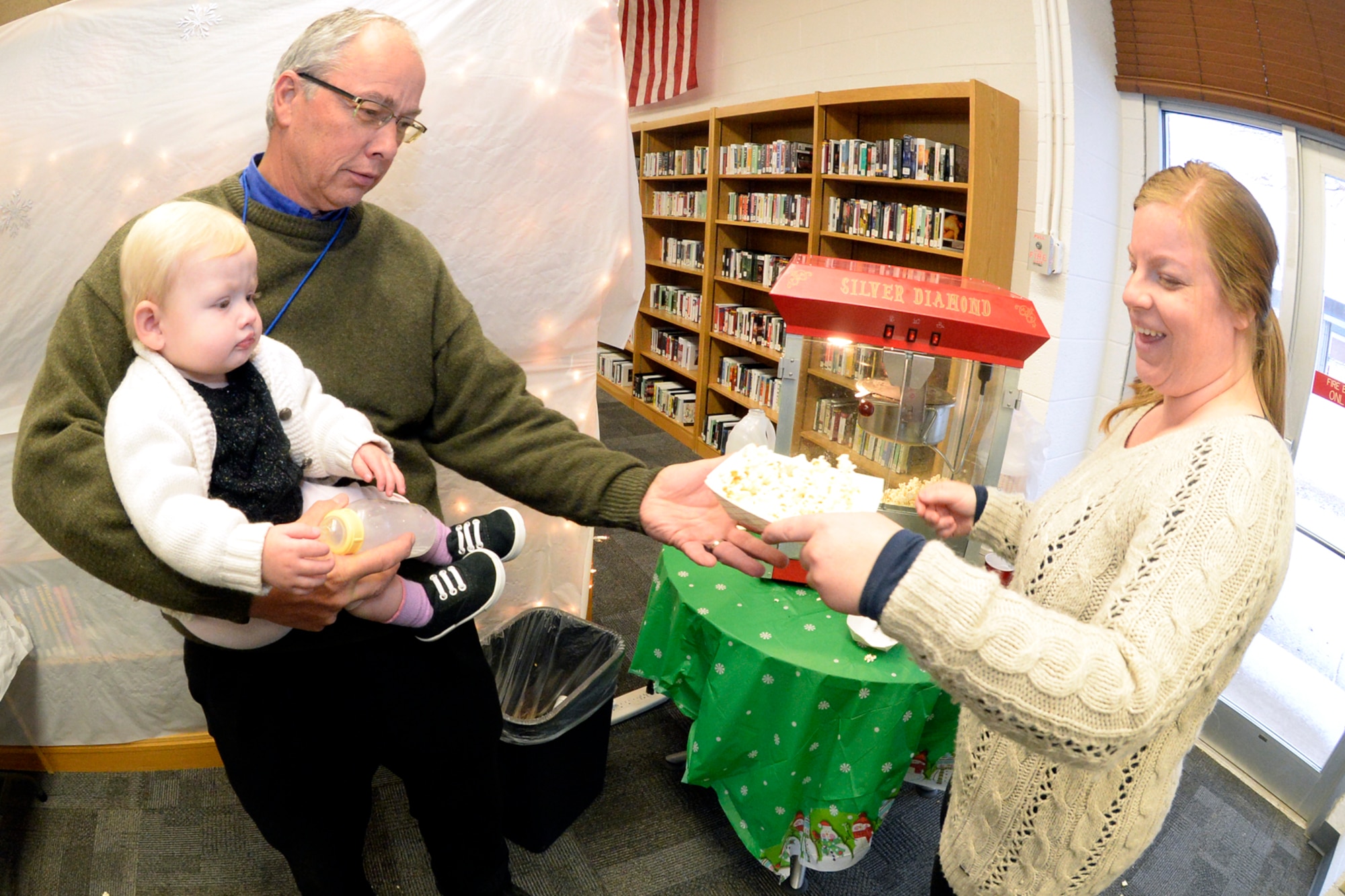 Jim Quist, holding Loddy Rogers, receives a popcorn snack from Heather Straub at the Hill Air Force Base Library, Dec. 8, 2016. (U.S. Air Force photo by Todd Cromar)