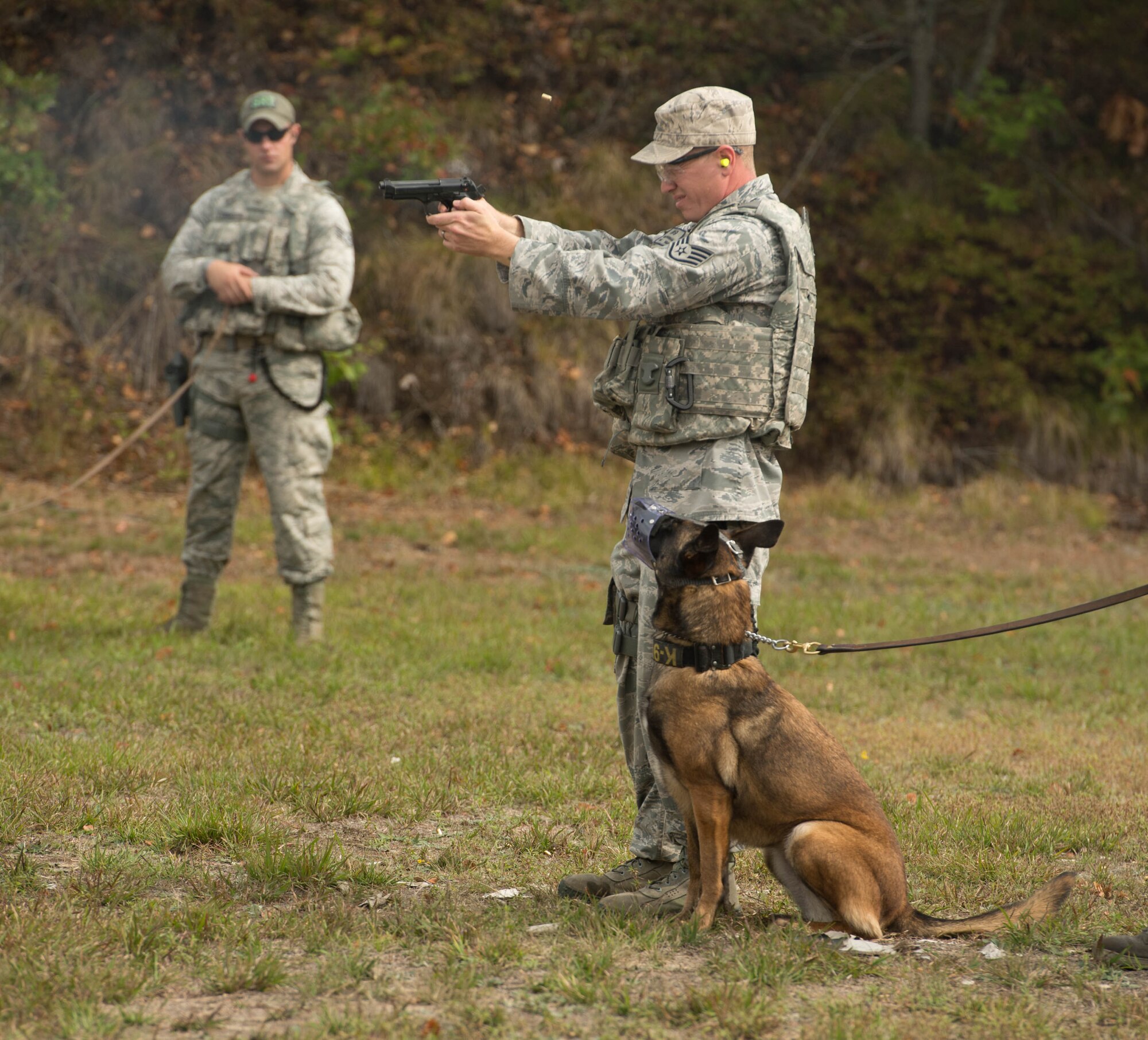 Staff Sgt. Adam Dunnam, 66th Security Forces Squadron Military Working Dog handler, fires his M9 pistol during live fire training at Fort Devens, Mass., Sept. 27, while Staff Sgt. Charles Cornacchio, 66 SFS MWD handler, and MWD Qquail, watch. Members of the security forces participated in the live fire training with their military working dog counterparts. (U.S. Air Force photo by Jerry Saslav)