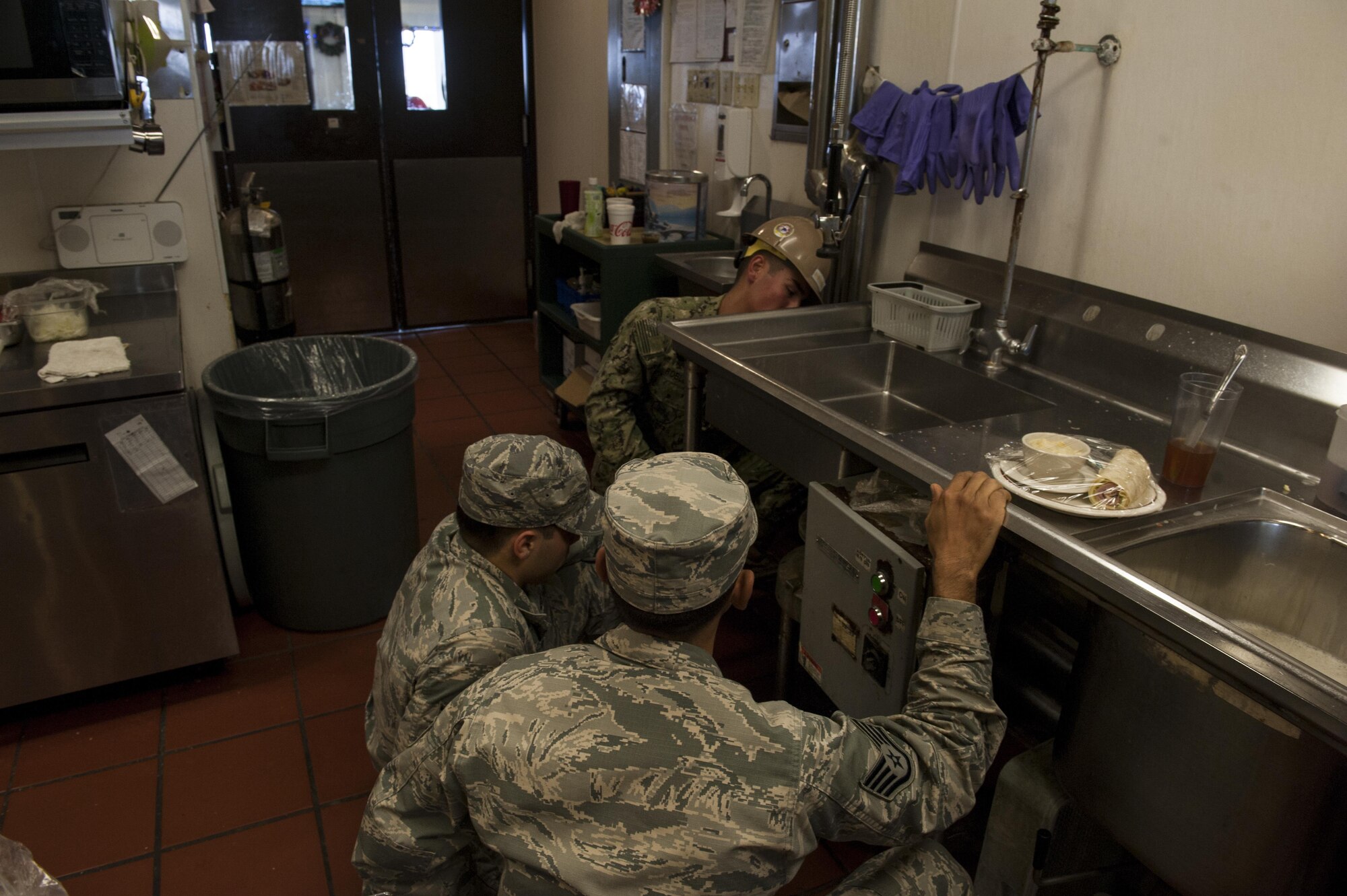 U.S. Air Force Staff Sgt. Jaime Gracias and Senior Airman Jacob Graham, 18th Civil Engineer Squadron Water and Fuels System Maintenance technicians, and U.S. Navy Seaman Richard Robledo, Naval Mobile Construction Battalion Five utilities construction man, take out an old garbage disposal unit at the Tee House Dec. 7, 2016, at Kadena Air Base, Japan. The WFSM technicians ensure different systems, such as garbage disposals, water systems for housing and plumbing are functioning properly or replaced entirely for safety. (U.S. Air Force photo by Senior Airman Lynette M. Rolen)