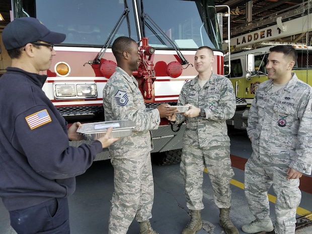 Master Sgt. Travis Heath, 628th Civil Engineer Squadron first sergeant, left, hands cookies to members of the fire department Dec. 7, 2016. The cookies were made by the Team Charleston Spouses Club for the annual holiday program: Operation Cookie Drop.