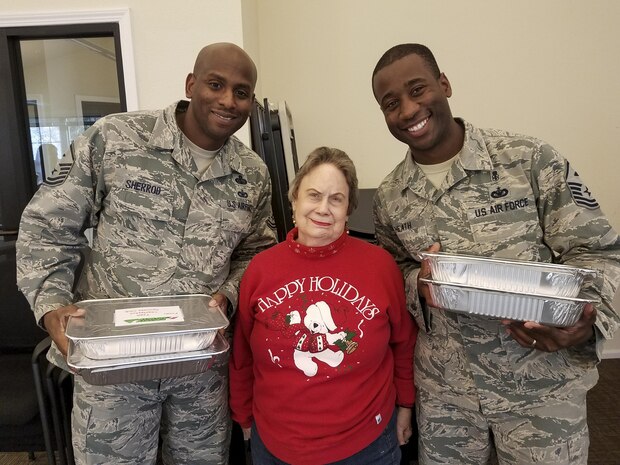 Master Sgt. Derrick Sherrod, 437th Maintenance Squadron first sergeant, left, and Master Sgt. Travis Heath, 628th Civil Engineer Squadron first sergeant, right, stand with June Griggs, Team Charleston Spouses Club member, when receiving cookies at the Hunt Housing Office Dec. 7, 2016. The cookies were made for the annual holiday program: Operation Cookie Drop where spouses baked cookies for Joint Base Charleston members working the mid, swing and night shifts.