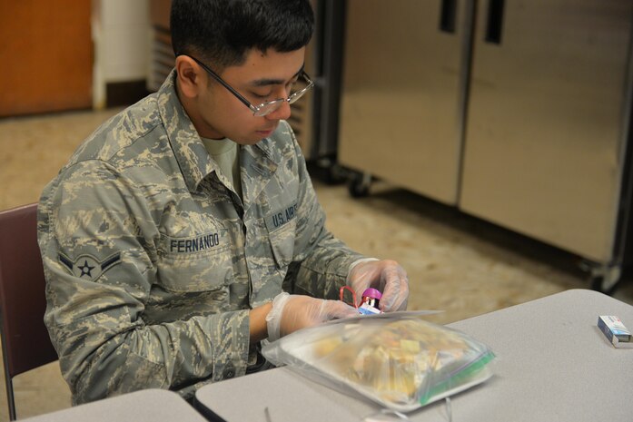 Airman Sean Fernando, 57th Maintenance Squadron, precision measurement equipment laboratory apprentice, staples a holiday card on a plate of cookies in the chapel basement on Nellis Air Force Base, Nev., Dec. 15. The holiday cookie drive is an annual base-wide event coordinated entirely by volunteers. (U.S. Air Force photo by Senior Airman Rachel Loftis)