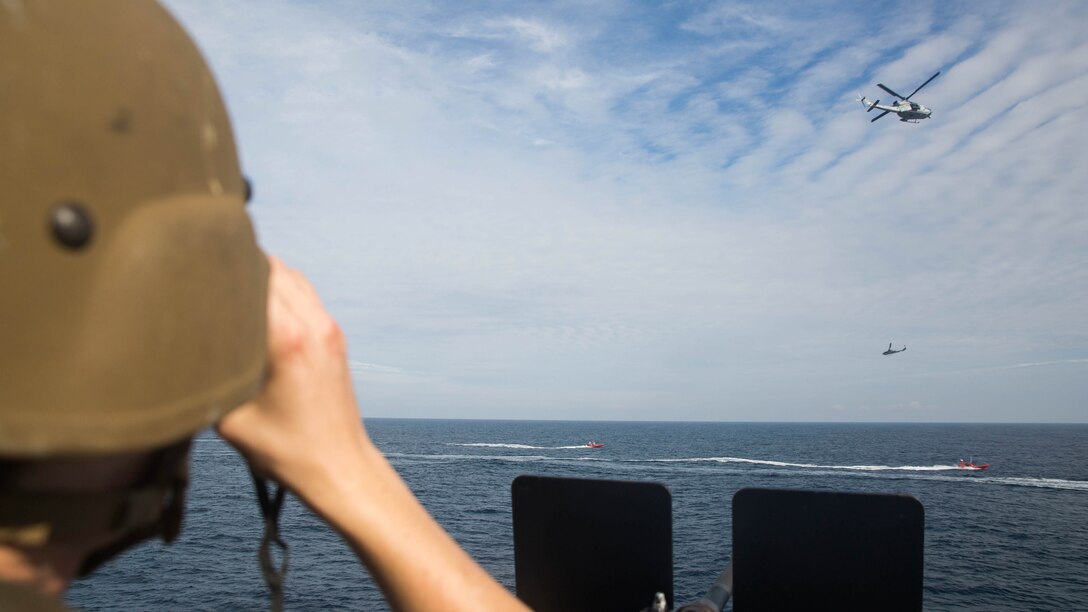 A sailor with the small caliber arms team observes 24th Marine Expeditionary Unit aircraft circling fast attack crafts off the starboard side of USS Mesa Verde (LPD 19), during a simulated straight transit to rehearse a defense of the amphibious task force mission during Amphibious Ready Group Marine Expeditionary Unit Exercise Dec. 13, 2016. During the three-week training evolution, Marines will tackle a wide range of operations and scenarios enhancing interoperability and amphibious warfare capabilities with their Navy counterparts. The additional firepower Marines provide improves the Navy-Marine Corps team’s ability to defend the naval vessels of the Bataan Amphibious Ready Group. 