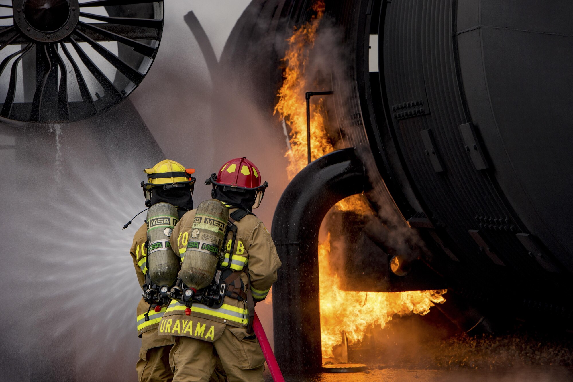 Two firefighters with the 374th Civil Engineer Squadron spray down a simulated aircraft fire during a live fire training exercise on Dec. 14, 2016, at Yokota Air Base, Japan. During the training the firefighters were split into three teams of two, with two teams extinguishing the fires and the remaining team on standby providing a safety line to help the primary teams. (U.S. Air Force photo by Airman 1st Class Donald Hudson)