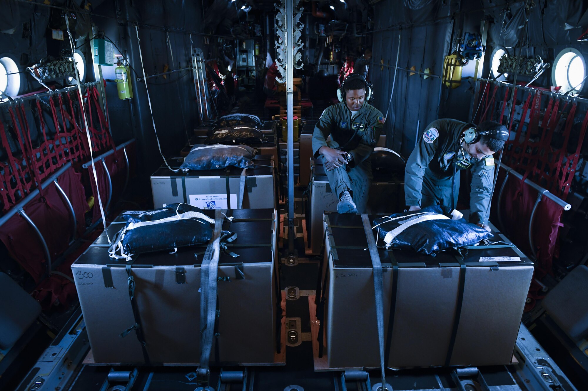Senior Airman Angel Torres, right, 36th Airlift Squadron loadmaster, is observed by Senior Airman Demore Rogers, 36 AS loadmaster, as he makes sure a bundle of donated goods is properly secured over the Pacific Ocean, Dec. 6, 2016. This year marks the 65th year of Operation Christmas Drop, which began in 1952, making it the world's longest-running airdrop mission. (U.S. Air Force photo by Senior Airman Elizabeth Baker)