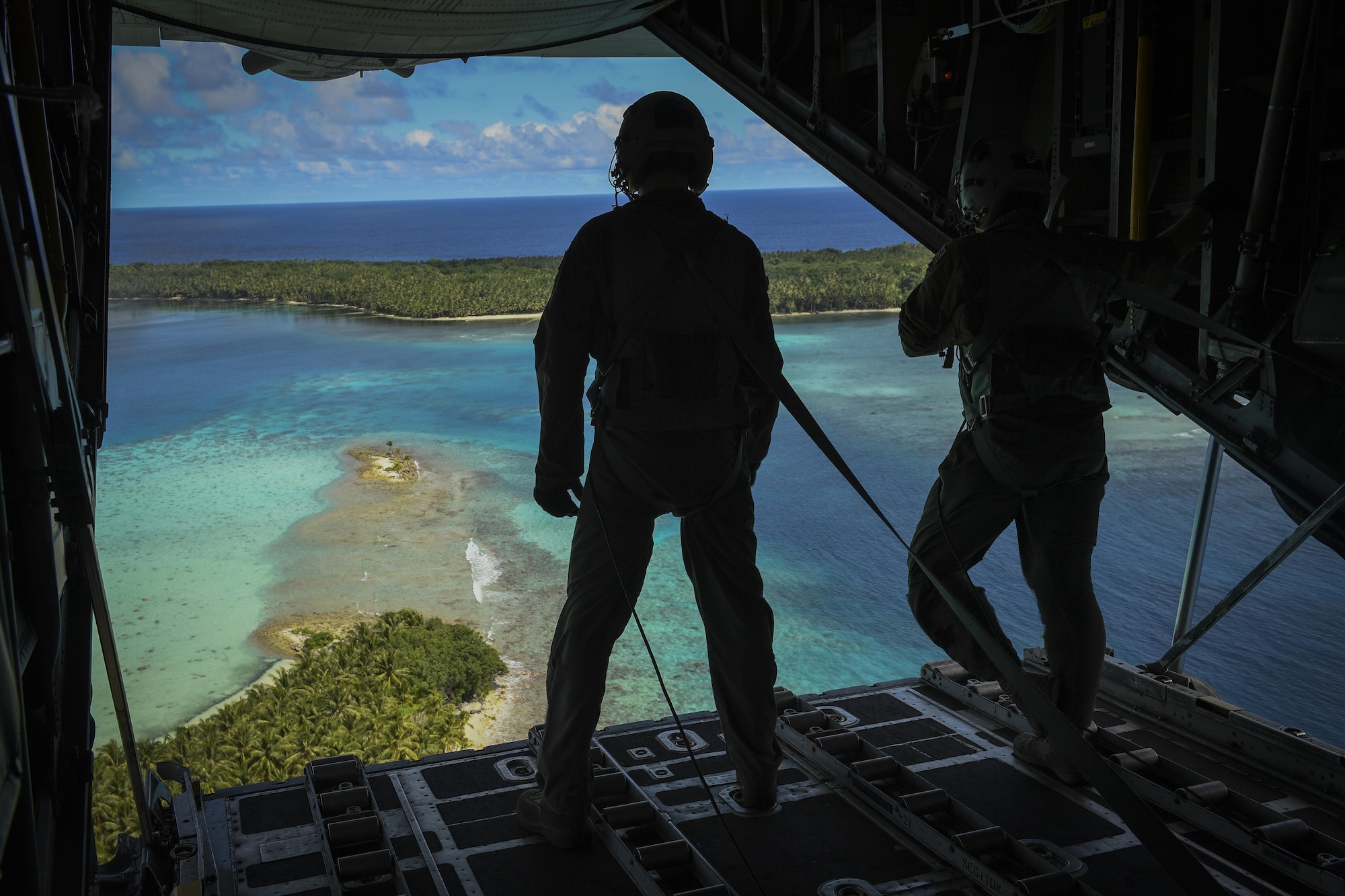 Senior Airman Nicholas Oswald, left, 36th Airlift Squadron C-130H loadmaster, and Tech. Sgt. Jonathan Lange, 36 AS C-130H Hercules instructor loadmaster, stand on the loading ramp after dropping bundles of donated goods over the Pacific islands during Operation Christmas Drop 2016, Dec. 11, 2016. The aircrew dropped bundles of food, supplies and gifts over the Micronesian Islands. Each year OCD provides aid to over 30,000 islanders in Chuuk, Palau, Yap, Marshall Islands and the Commonwealth of the Northern Mariana Islands. (U.S. Air Force photo by Senior Airman Elizabeth Baker)