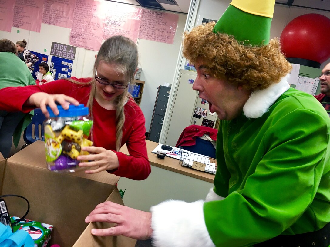 Buddy the Elf, played by Master Sgt. Daron Nelson from the 67th Aerial Port Squadron, watches Avonlea open gifts during a Christmas party for students with special needs at Mound Fort Junior High in Ogden Dec. 16. The 67th APS has hosted the party annually for nearly 30 years, providing gifts, clothes, and hygiene items. (U.S. Air Force photo)