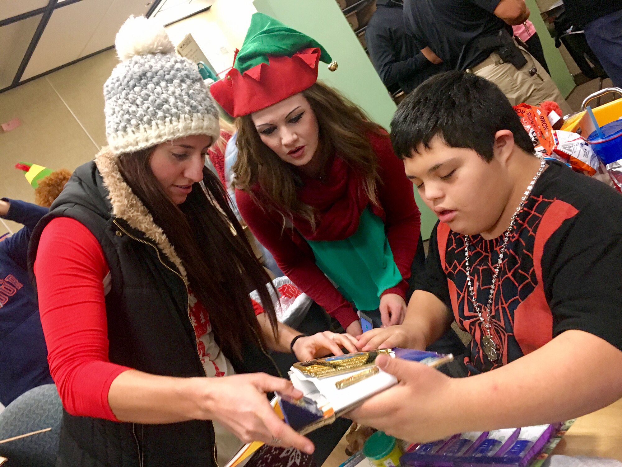 Tech. Sgt. Sara Kunze and Senior Master Sgt. Jodi Kozy, 67th Aerial Port Squadron, unwrap presents with Mound Fort Junior High student Tony. For nearly 30 years, the 67th APS has hosted the annual party for students with special needs, providing gifts, clothes, and hygiene items. (U.S. Air Force photo)