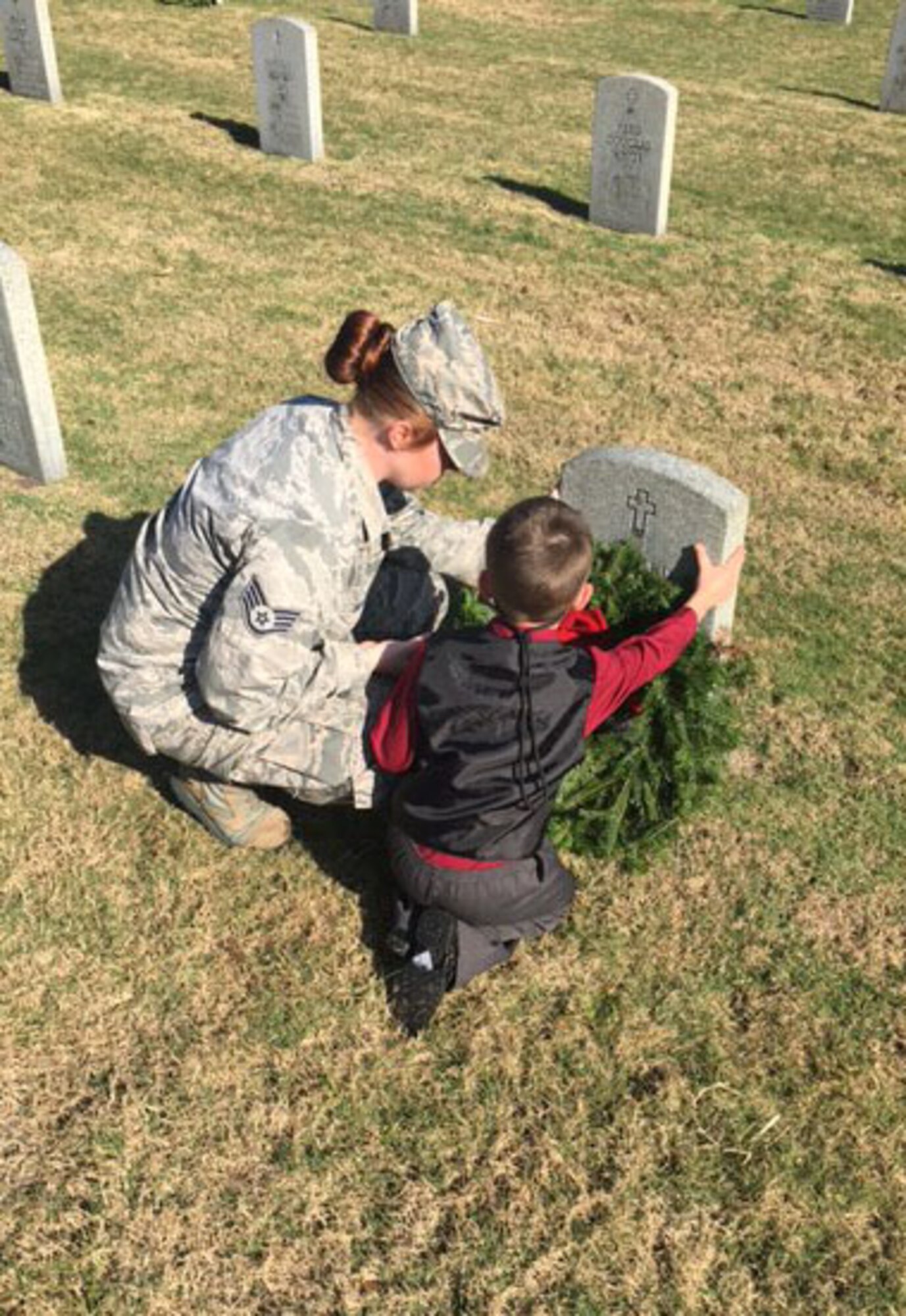 Staff Sgt. Brittany Liddon, NCO in charge of Community Relations assigned to the 6th Air Mobility Wing Public Affairs office, and her son, Easton, place a wreath on a gravesite at Florida National Cemetery in Bushnell, Fla., Dec. 17, 2016. Liddon and her son participated in the 11th Annual Wreath Laying Ceremony at Florida National Cemetery to honor fallen service members. (U.S. Air Force photo by Senior Airman Tori Schultz)
