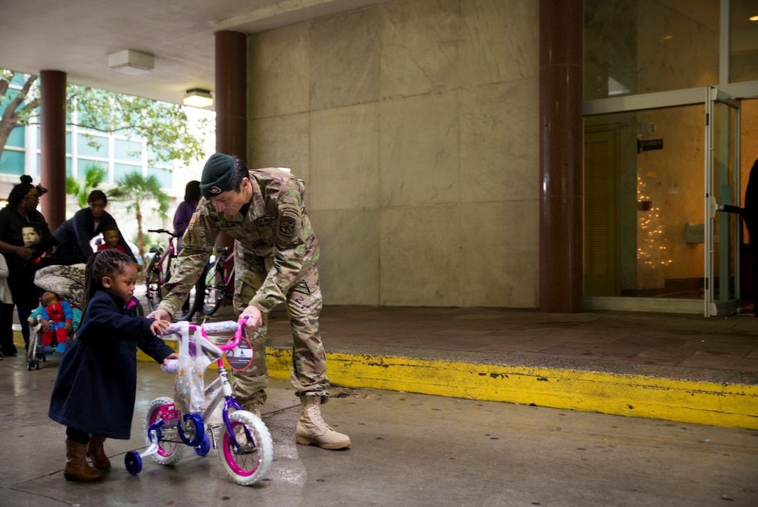 U.S. Army Maj. Manuel Acosta helps a young child move the brand new bicycle she received during the Zulu Social Aid and Pleasure Club’s annual Toys for Tots distribution at New Orleans City Hall, Dec. 17, 2016. Nearly 2,000 families lined up to receive toys and gifts. Toys for Tots, an annual Marine Corps Reserve program, aims at collecting new, unwrapped Christmas gifts for less fortunate children in the community. Since its inception in 1947, Toys for Tots has distributed 512 million toys to 237 million children.