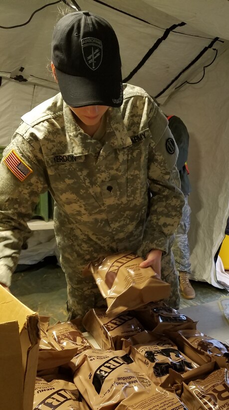 Spc. Savannah Yerdon, a culinary specialist assigned to the 1018th Quartermaster Company in Schenectady, N.Y., stacked MREs on a table prior to Soldiers filing into the DFAC tent for breakfast at Fort Bragg, N.C., Luzon Drop Zone on 12 Dec., 2016. Yerdon was part of a six person food service crew who provided meal rations for hundreds of Soldiers during Operation Toy Drop XIX. (U.S. Army photo by Capt. Ebony Malloy)