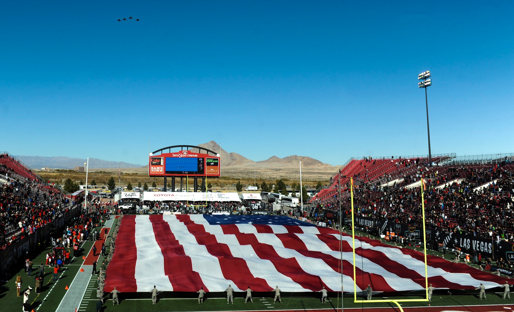 Four F-16 Fighting Falcons perform a fly-over as Airmen from Nellis and Creech Air Force Bases hold the American flag at Sam Boyd Stadium during the Las Vegas Bowl, Dec. 17, 2016. The F-16s flew over the stadium as the National Anthem played before the game began. (U.S. Air Force photo by Airman 1st Class Kevin Tanenbaum/Released)