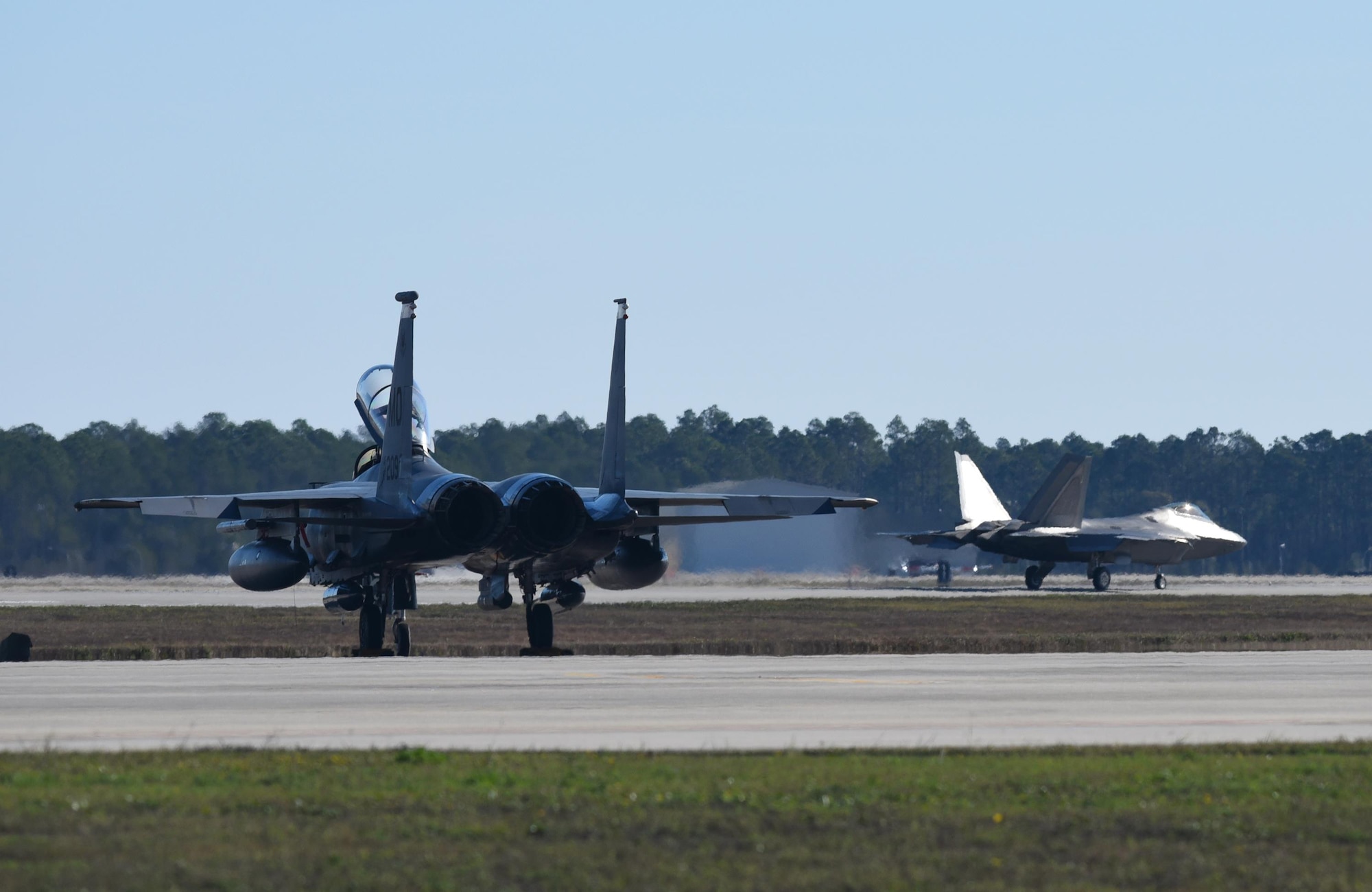 A U.S. Air Force F-15E Strike Eagle from Mountain Home Air Force Base, Idaho, sits at the ready while a Tyndall F-22 Raptor passes during Checkered Flag 17-1 at Tyndall Air Force Base, Fla., Dec. 16, 2016. During the exercise, fourth- and fifth-generation fighter pilots worked together to complete missions involving multiple airframes including the F-35A Lightning II, F-22, F-16CM Fighting Falcon, F-15E Strike Eagle, HH-60G Pave Hawk and  E-3 Sentry airframes. (U.S. Air Force photo by Staff Sergeant Alex Fox Echols III/Released)