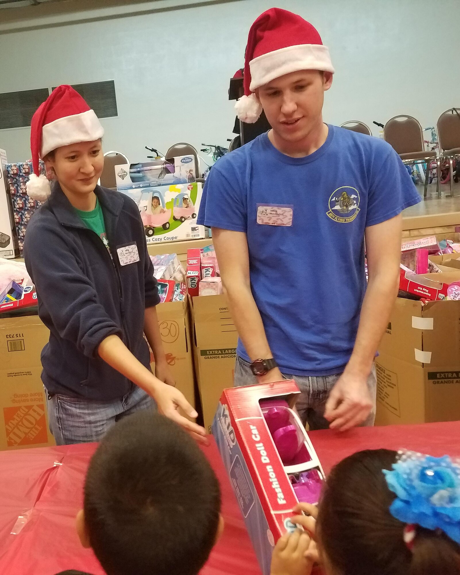 1st Lt. Kimberly Jackson and Capt. Logan Suhr, members of the 85th Flying Training Squadron, present gifts to two youngsters at Niños Navideños, a charity, at the Del Rio Civic Center in Del Rio, Texas, Dec. 17, 2016. Volunteers, many from Laughlin, presented 1,300 toys and 80 bicycles to children at the event.  The event began in 2004 and has grown every year. (U.S. Air Force photo/Joel Langton)