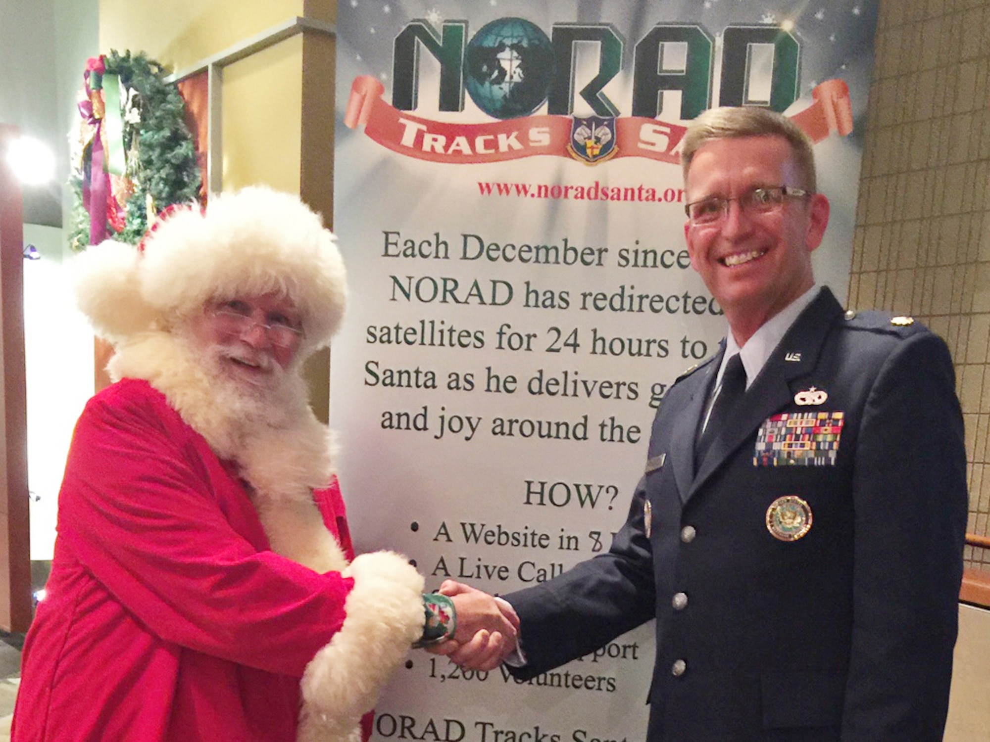 Lt. Col. Karl Fruendt shakes hands with Santa Claus at a NORAD Tracks Santa event. Lt. Col. Karl Fruendt is the voice behind the English-language videos on the NORAD Tracks Santa website and is also part of local holiday performances, narrating the history of the NORAD-run service. (Courtesy photo)