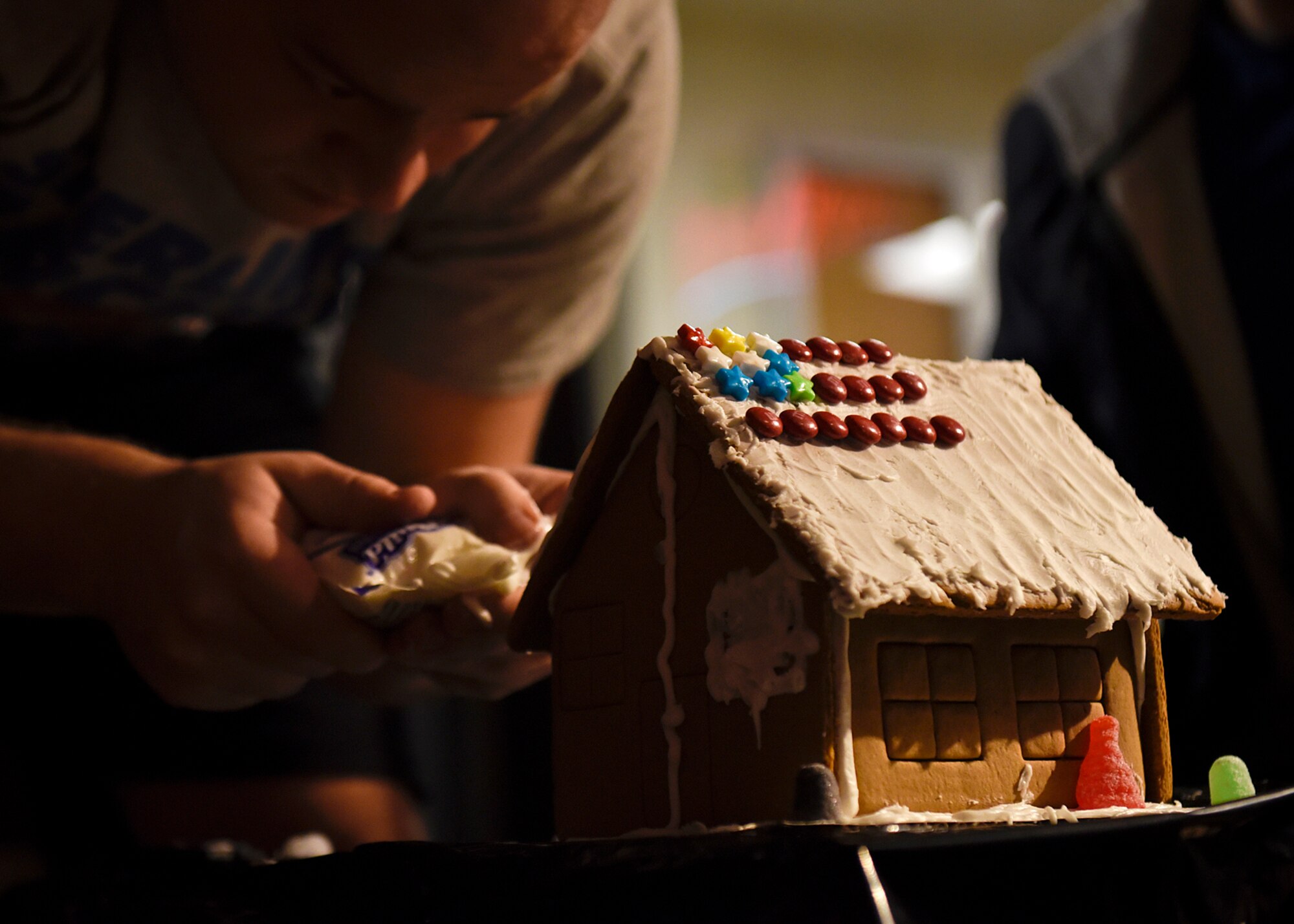 PETERSON AIR FORCE BASE, Colo. – Drake Smith, Eclipse Cyber Café barista, works to add a dinosaur on his submission for the 4th Annual Gingerbread House Building Competition put on by the Peterson Chapel at the Eclipse Cyber Café on Peterson Air Force Base, Colo., Dec. 14, 2016. The contest followed a free meal provided by the chapel, a weekly event at the café. (U.S. Air Force photo by Senior Airman Rose Gudex))