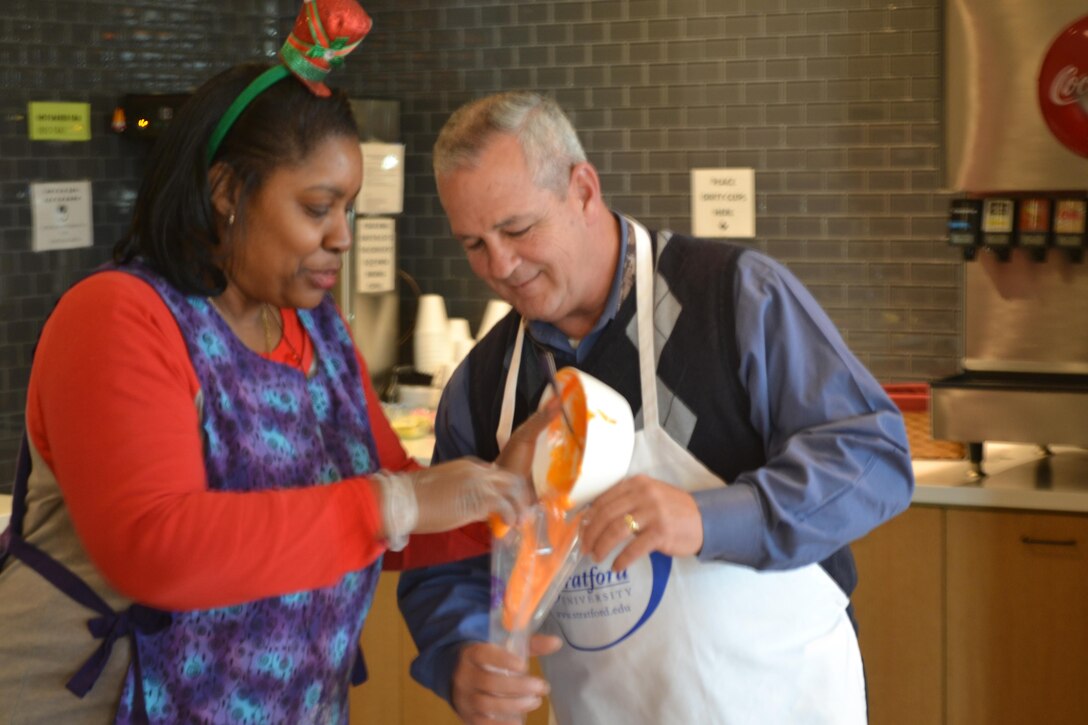 Dorothy Russell and Dennis Ross of DLA Logistics Operations Disposal Policy and Compliance Division add decorative topping to a frosting bag. The group provided its own ingredients and even mixed the toppings from scratch.