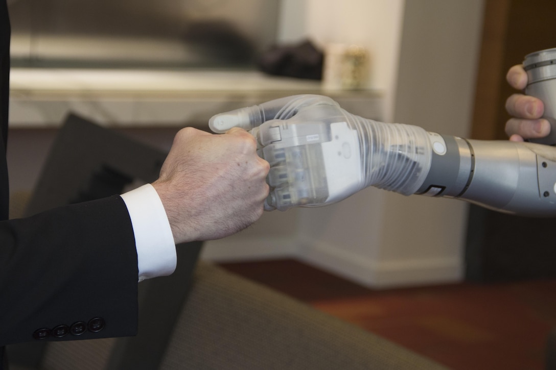 Dr. Justin Sanchez, director of the Defense Advanced Research Projects Agency’s Biological Technologies Office, fist-bumps with one of the first two advanced “LUKE” arms to be delivered from a new production line during a ceremony at Walter Reed National Military Medical Center in Bethesda, Md., Dec. 22, 2016 DoD photo