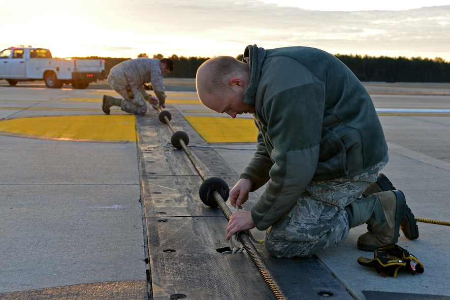 U.S. Air Force Staff Sgt. Timothy Shearer, left, and Airman 1st Class Travis Green, right, 20th Civil Engineer Squadron power production craftsman and apprentice, tie down an aircraft arresting system cable at Shaw Air Force Base, S.C., Dec. 23, 2016. The power production flight is responsible for maintaining and replacing the aircraft arresting systems, which help keep 20th Fighter Wing pilots safe in the event of an emergency. (U.S. Air Force photo by Airman 1st Class Destinee Sweeney)