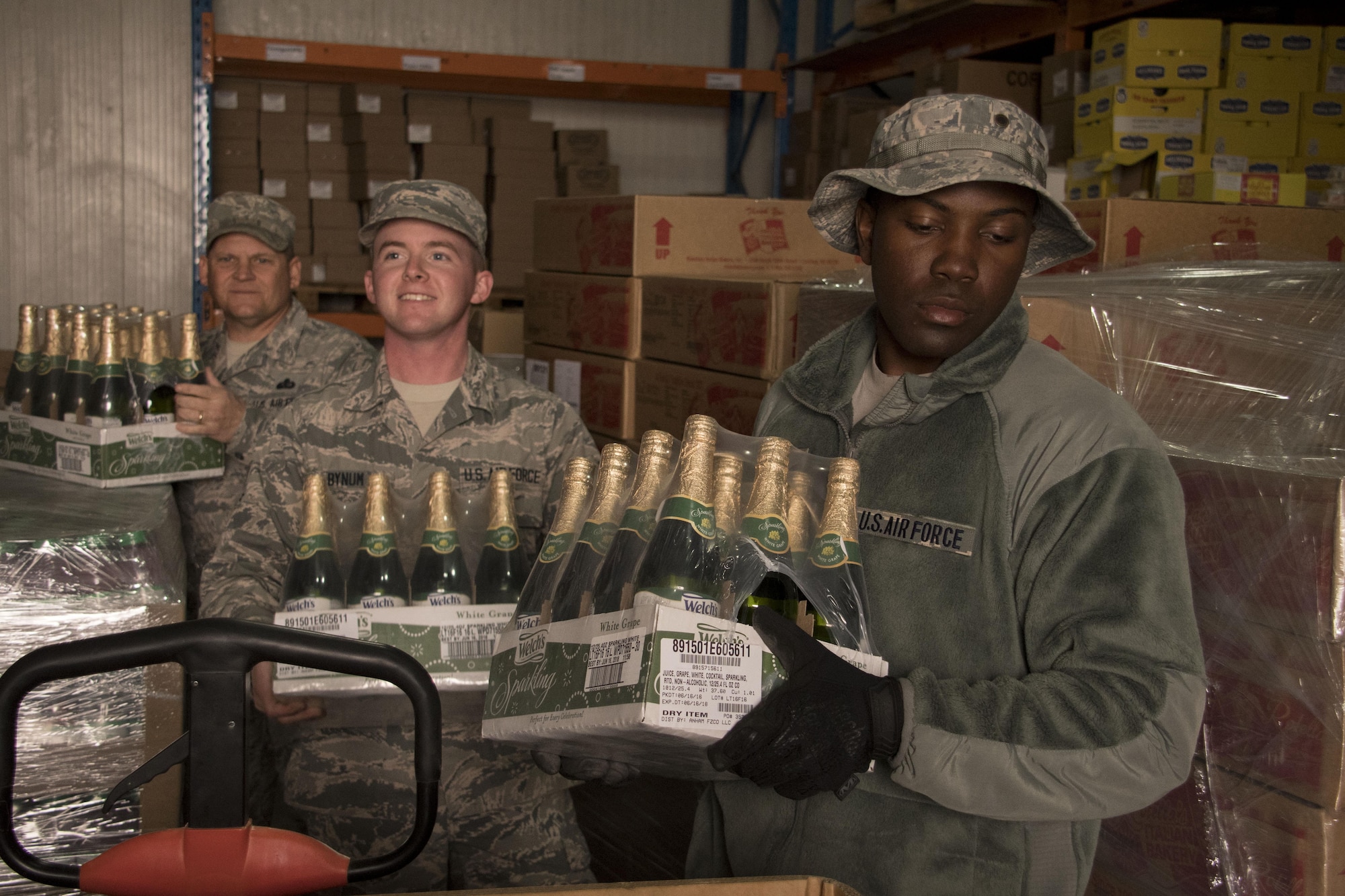 Airmen from the 386th Expeditionary Force Support Squadron carry sparkling grape juice through a storeroom Dec. 22, 2016 at an undisclosed location in Southwest Asia. These Airmen were assembling tri-walls of holiday meal items for forward-deployed service members (U.S. Air Force photo/Senior Airman Andrew Park)