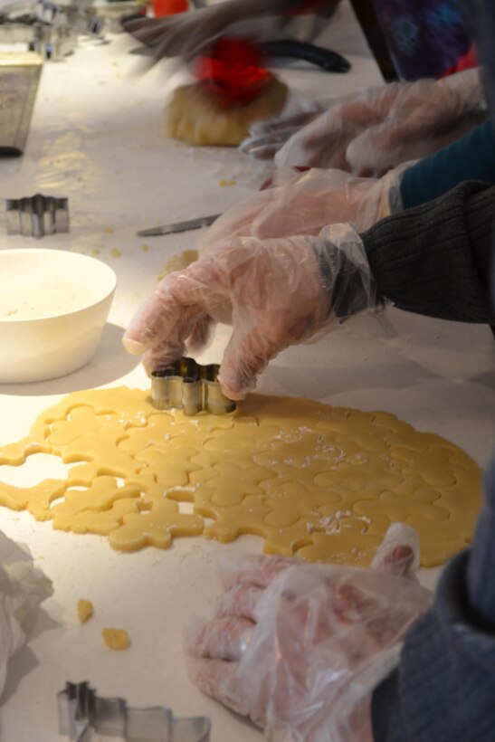 Team members cut freshly kneaded dough into holiday shapes before baking the cookies.