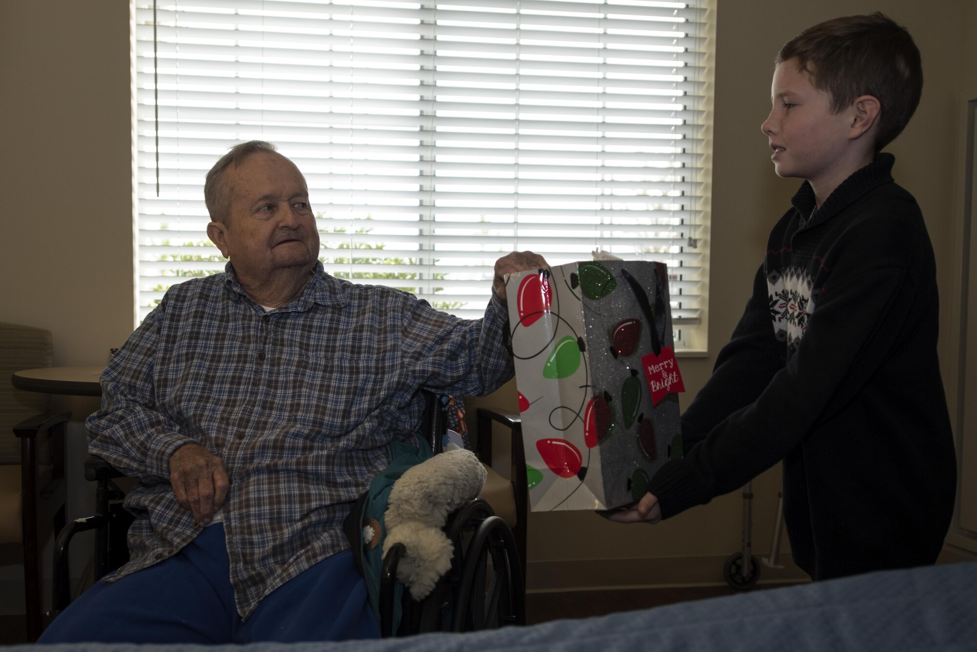 Lyman Sauls (left), U.S. Army veteran and resident of North Carolina State Veterans Home, receives a gift bag from the son of Col. Christopher Sage, 4th Fighter Wing commander, Dec. 24, 2016, in Kinston, North Carolina. More than 90 residents were visited and received a goody bag and holiday card. (U.S. Air Force photo by Airman Shawna L. Keyes)