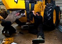 (From left) Airmen 1st Class Brennan Walley and Rodrigo Salgado, 5th Logistics Readiness Squadron vehicle maintenance technicians, install hydraulic lines on a grader vehicle at Minot Air Force Base, N.D., Dec. 14, 2016. These Airmen work on various components of government vehicles, such as electrical systems, brakes, transmissions, and heating and cooling systems. (U.S. Air Force photo/Airman 1st Class Jonathan McElderry)