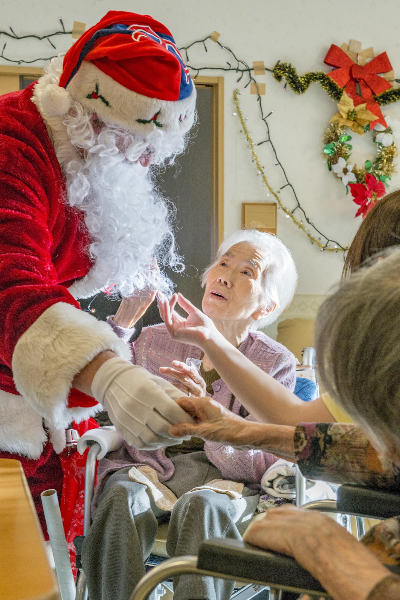 Residents of the Fussa Kotobuki Garden Nursing Home shake hands and feel Santa Claus’ beard during a Christmas Eve visit on Dec. 24, 2016, in Fussa, Tokyo, Japan. Volunteers from Yokota Air Base’s Community Center Outreach Program visit the Kotobuki Garden Nursing Home multiple times a year to visit with the residents to provide positive and caring outreach opportunities in the local community. (U.S. Air Force photo by Airman 1st Class Donald Hudson)