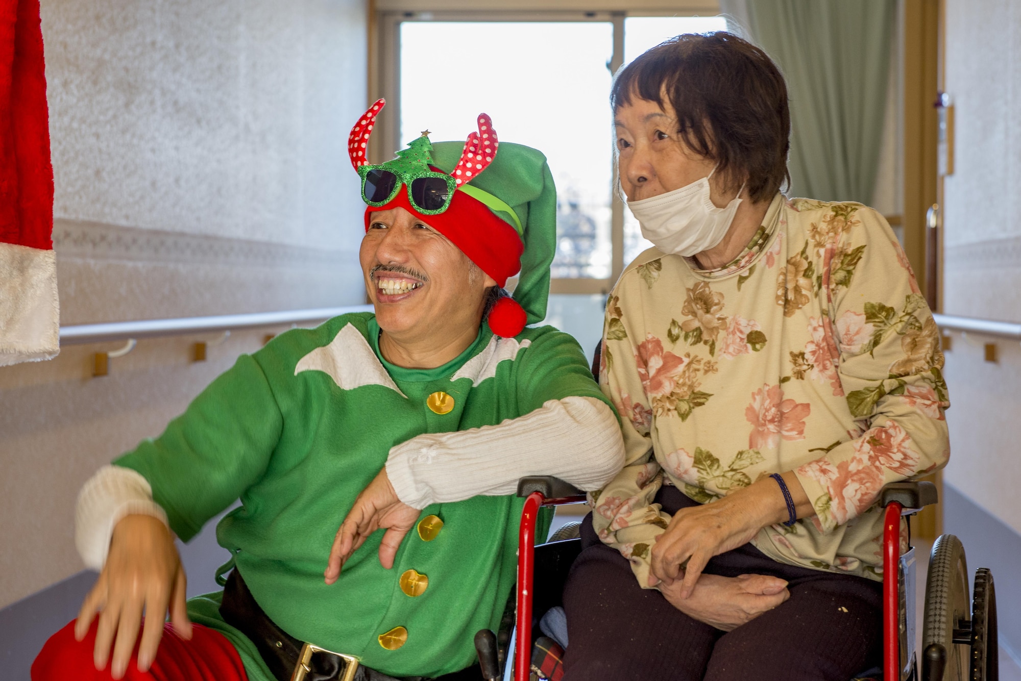 A resident of the Fussa Kotobuki Garden Nursing Home and a volunteer wait for Santa Claus during a Christmas Eve visit on Dec. 24, 2016, in Fussa, Tokyo, Japan. During visits throughout the years to the Fussa Kotobuki Garden Nursing Home, volunteers have arranged various activities such as the Christmas Eve visits, barbecue lunches, taking residents for walks along the nearby Tama River or going to simply sit and talk with them. (U.S. Air Force photo by Airman 1st Class Donald Hudson)