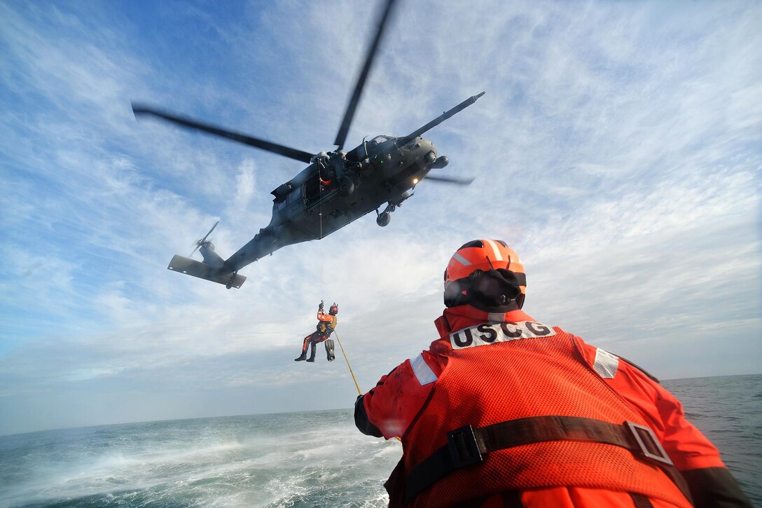 Coast Guard Petty Officer 2nd Class Benjamin Esposita, foreground, helps with the hoist line from an HH-60 Pave Hawk helicopter during training in the waters near Coast Guard Station Shinnecock in Hampton Bays, N.Y., Dec. 22, 2016. Esposita is a machinery technician. Air National Guard photo by Staff Sgt. Christopher S. Muncy
