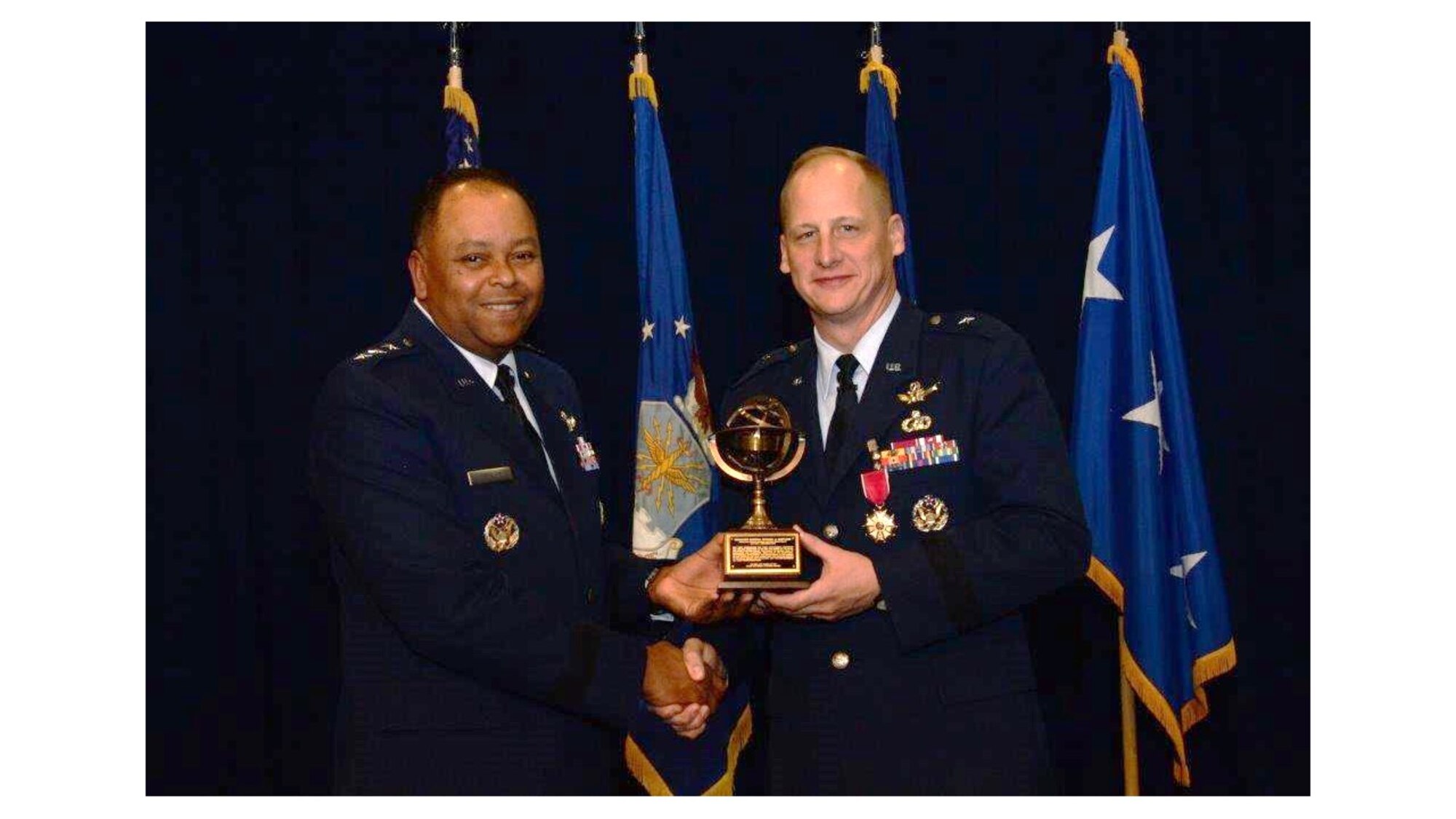 Lt. Gen. Samuel Greaves, commander of the Space and Missile Systems Center, and program executive officer for Space presents Brig. Gen. Michael Guetlein with a miniature replica of the SMC Armillary sculpture in recognition of his leadership at the center Dec. 19, during a change of leadership ceremony in the Gordon Conference Center of the Schriever Space Complex at Los Angeles Air Force Base in El Segundo, Calif.  General Guetlein, the departing Senior Material Leader of the RS Directorate, leaves SMC to become the program executive for programs and integration at the Missile Defense Agency in Huntsville, Alabama. (U.S. Air Force photo/Van De Ha)