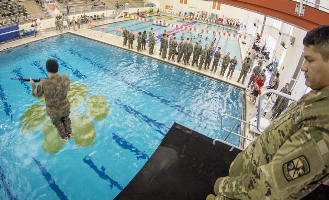 Army Master Sgt. Joe Medrano, right, watches as a cadet leaps blindfolded into a pool from a 5-meter diving platform carrying an M16 rifle during a combat water survival test at Clemson University, S.C., Jan. 28, 2016. Medrano is a senior military instructor assigned to Clemson University’s ROTC. Army photo by Staff Sgt. Ken Scar