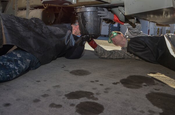 A member from the Naval Air Facility Atsugi Carrier Airborne Early Warning Squadron and an Airman with the 374th Logistics Readiness Squadron Fuels Management Flight hold a bucket to catch JP-8 fuel for an inspection at Yokota Air Base, Japan, Jan. 26, 2016. The Navy personnel who received training on the R-11 refueling trucks learned how to drive, service aircraft, perform minor maintenance and how to check fuel samples with the vehicle. (U.S. Air Force photo/Senior Airman David Owsianka)