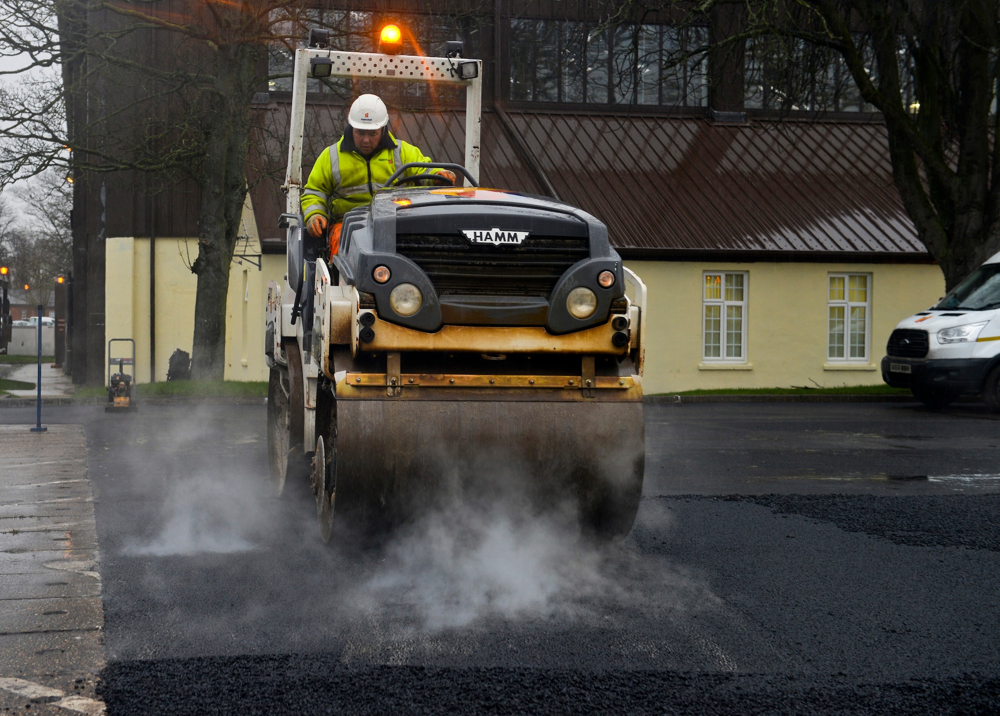 A contracted construction worker drives a steam roller over freshly laid asphalt in the 100th Logistics Readiness Squadron Vehicle Operations yard Jan. 22, 2016, on RAF Mildenhall, England. Construction workers used steam rollers to compact and even out the surface of the parking lot. (U.S. Air Force photo by Staff Sgt. Micaiah Anthony/Released) 