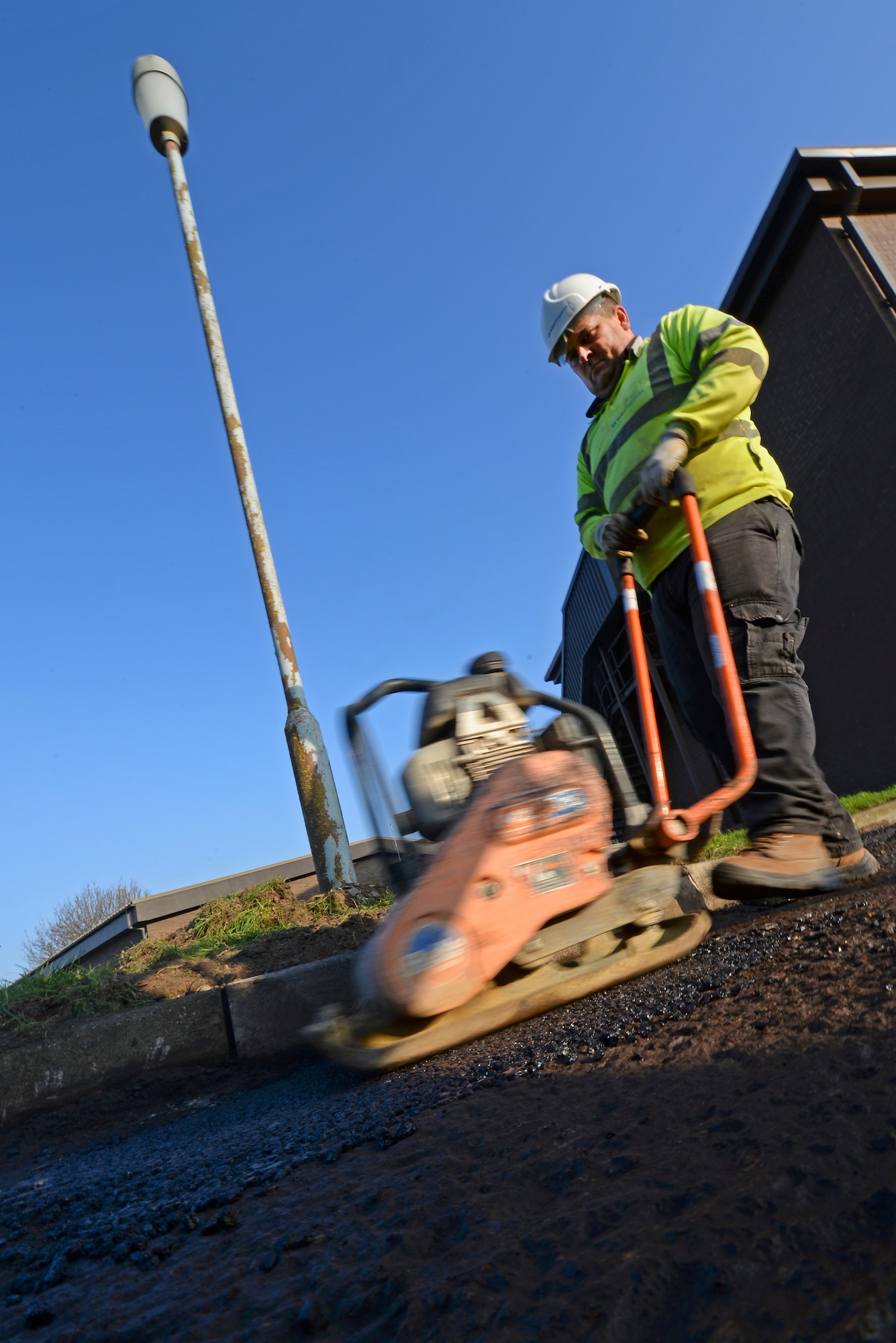 A contracted construction worker uses a plate tamper to compact asphalt in the 100th Logistics Readiness Squadron Vehicle Operations yard Jan. 20, 2016, on RAF Mildenhall, England. Workers filled uneven surfaces with tarmac and compacted it down to provide an even surface for the asphalt paver. (U.S. Air Force photo by Staff Sgt. Micaiah Anthony/Released))