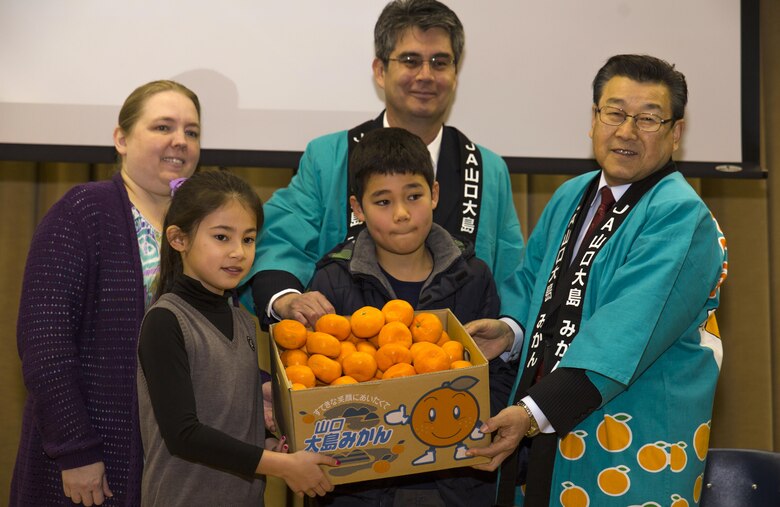 From left to right, Jenny Reese, assistant principal at Matthew C. Perry Elementary School, Jessica Blackston and Kenji Brunson, students at M.C. Perry Elementary School and Arturo Rivera, principal at M.C. Perry Elementary School receive a box of mikans from Motoi Yoshimura, right, leading board director and union president at the Yamaguchi Oshima Agricultural Cooperative Association during the 6th Annual Mikan Presentation at M.C. Perry at Marine Corps Air Station Iwakuni, Japan, Feb. 1, 2016. Mikans are orange citrus fruits that resemble tangerines and are a symbol of Japan’s agricultural export business. The event provided students and staff the opportunity to strengthen their bond with Iwakuni residents.