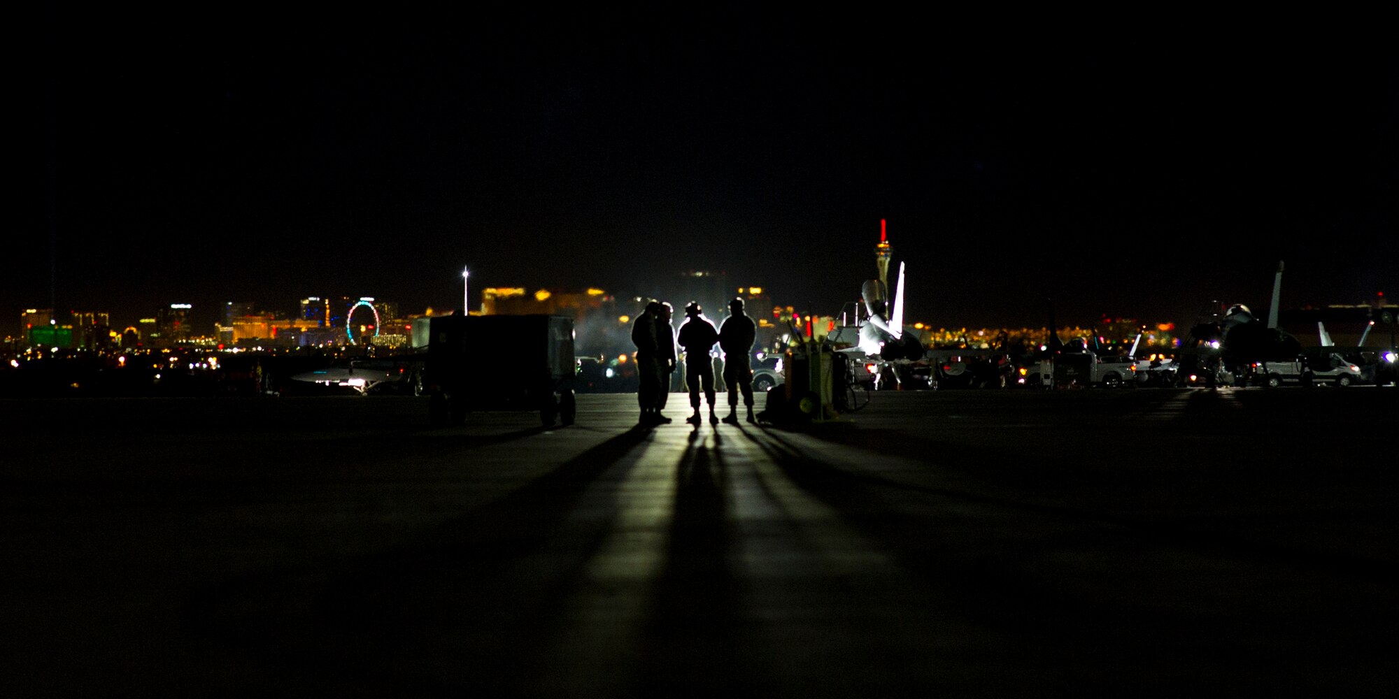 Four Airmen stand on the flightline looking toward the lights of Las Vegas Jan. 26, at Nellis AFB, Nev. The Airmen are part of more than 3,000 personnel from over 30 units including squadrons from Australia and the United Kingdom here to participate in Red Flag 16-1. (U.S. Air Force photo by Senior Airman Alex Fox Echols III/Released)  