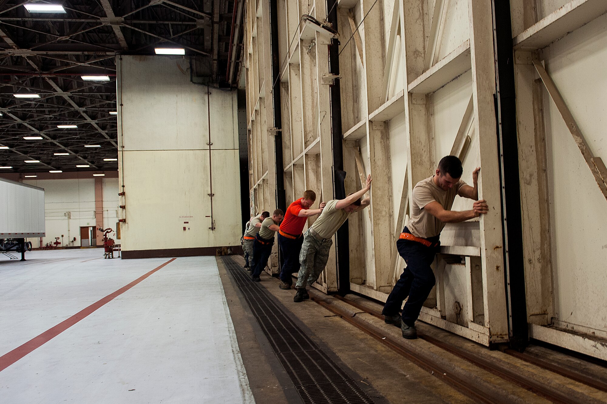 Members of 18th Equipment Maintenance Squadron push a hangar door open Jan. 29, 2016, at Kadena Air Base, Japan. The door was opened to allow a towing vehicle to enter the hangar and move a jet, taking at least six people to make an opening big enough to push a jet through. (U.S. Air Force photo by Airman 1st Class Corey M. Pettis)