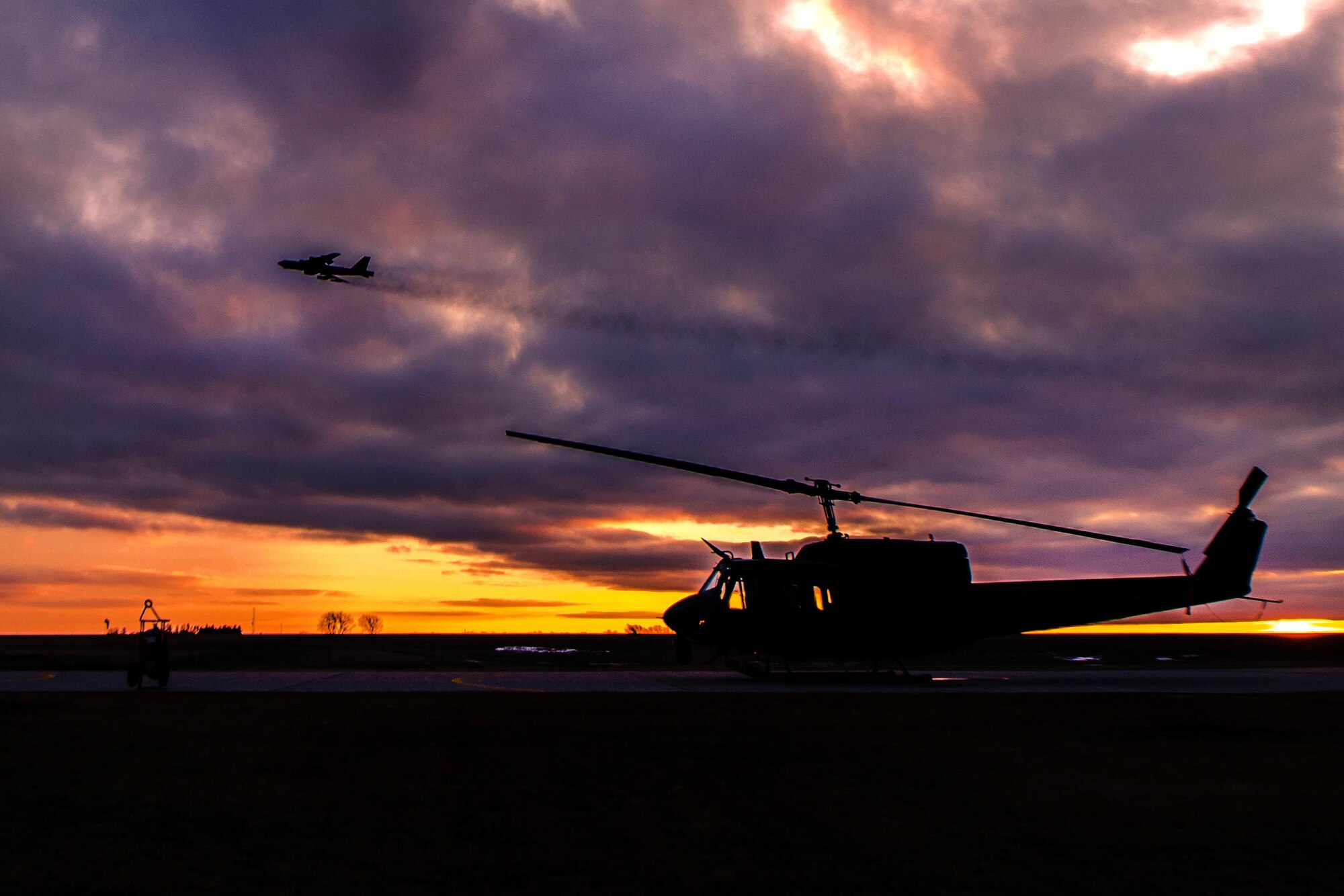 An aircraft flies over a UH-1N Iroquois helicopter on the helo-pad at Minot Air Force Base, N.D., Feb. 2, 2016. The helicopter is assigned to the 54th Helicopter Squadron. Air Force photo by Airman 1st Class J.T. Armstrong