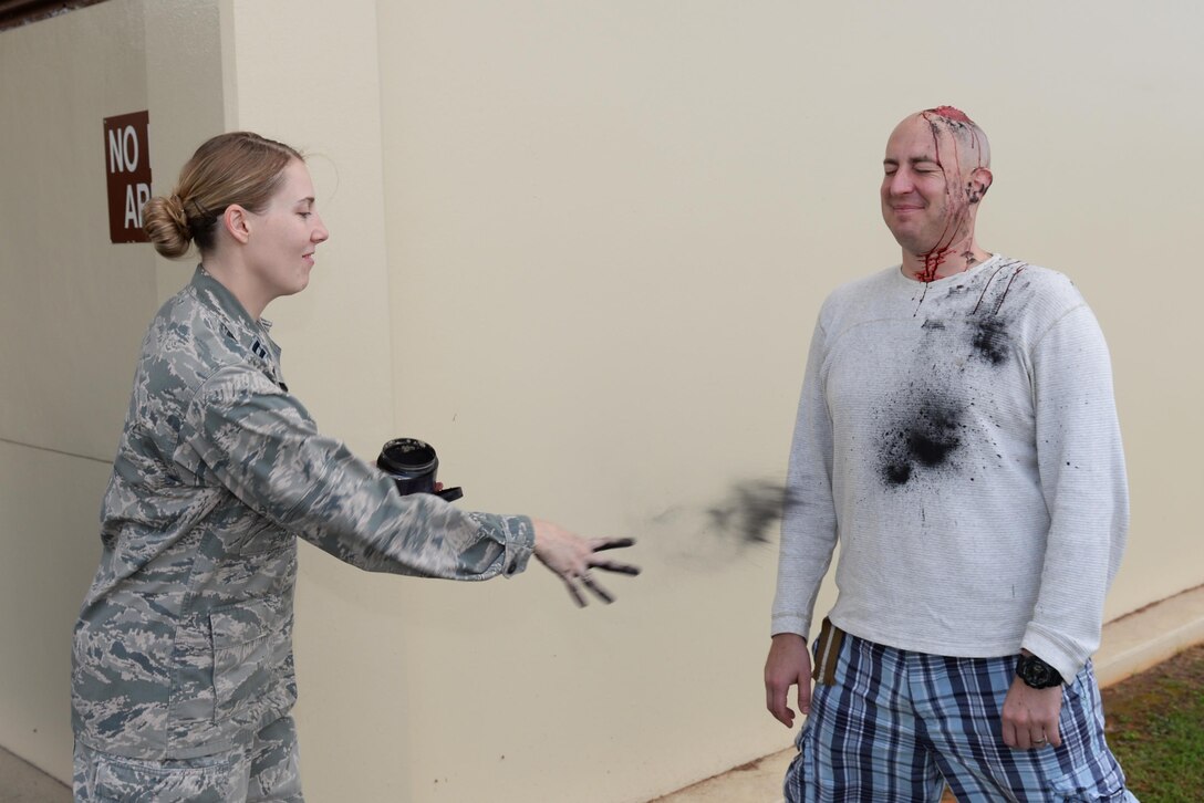 Capt. Kathryn Oja, 36th Medical Support Squadron medical readiness flight commander, tosses charcoal on Tech. Sgt. Eric Morris, 36th Mobility Response Squadron ramp coordinator, Feb. 3, 2016, at Andersen Air Force Base, Guam. Charcoal aims to mimic residue from burns and explosions caused by the simulated incident for the massive accident response exercise.  (U.S. Air Force photo/Airman 1st Class Jacob Skovo)