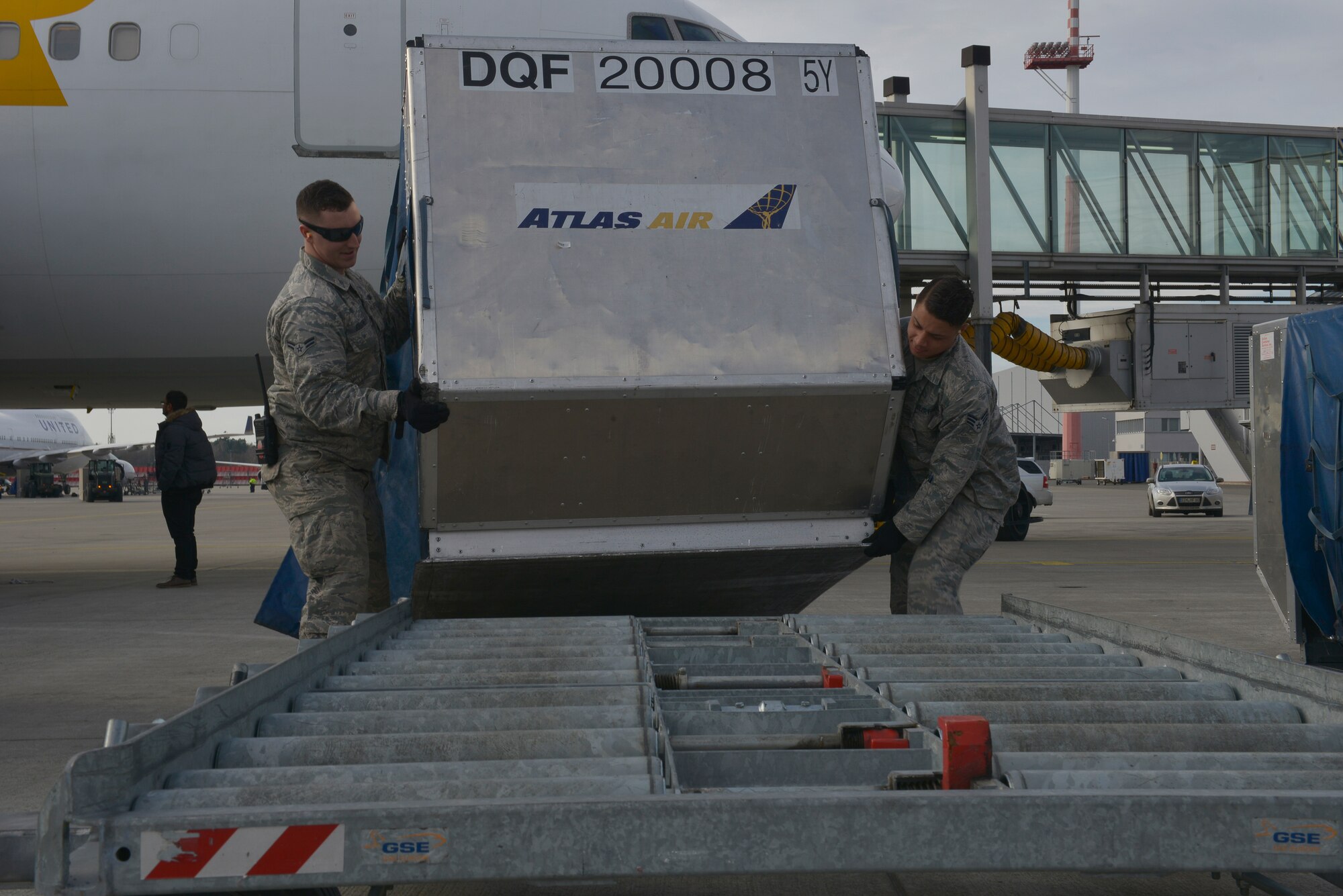 Senior Airman Cornel Griffen and Airman 1st Class Paul Boughner, 721st Aerial Port Squadron passenger service agents, load cargo containers onto a platform Jan. 27, 2016, at Ramstein Air Base, Germany. These platforms are used to quickly transport cargo around the flightline. (U.S. Air Force photo/Airman 1st Class Lane T. Plummer)