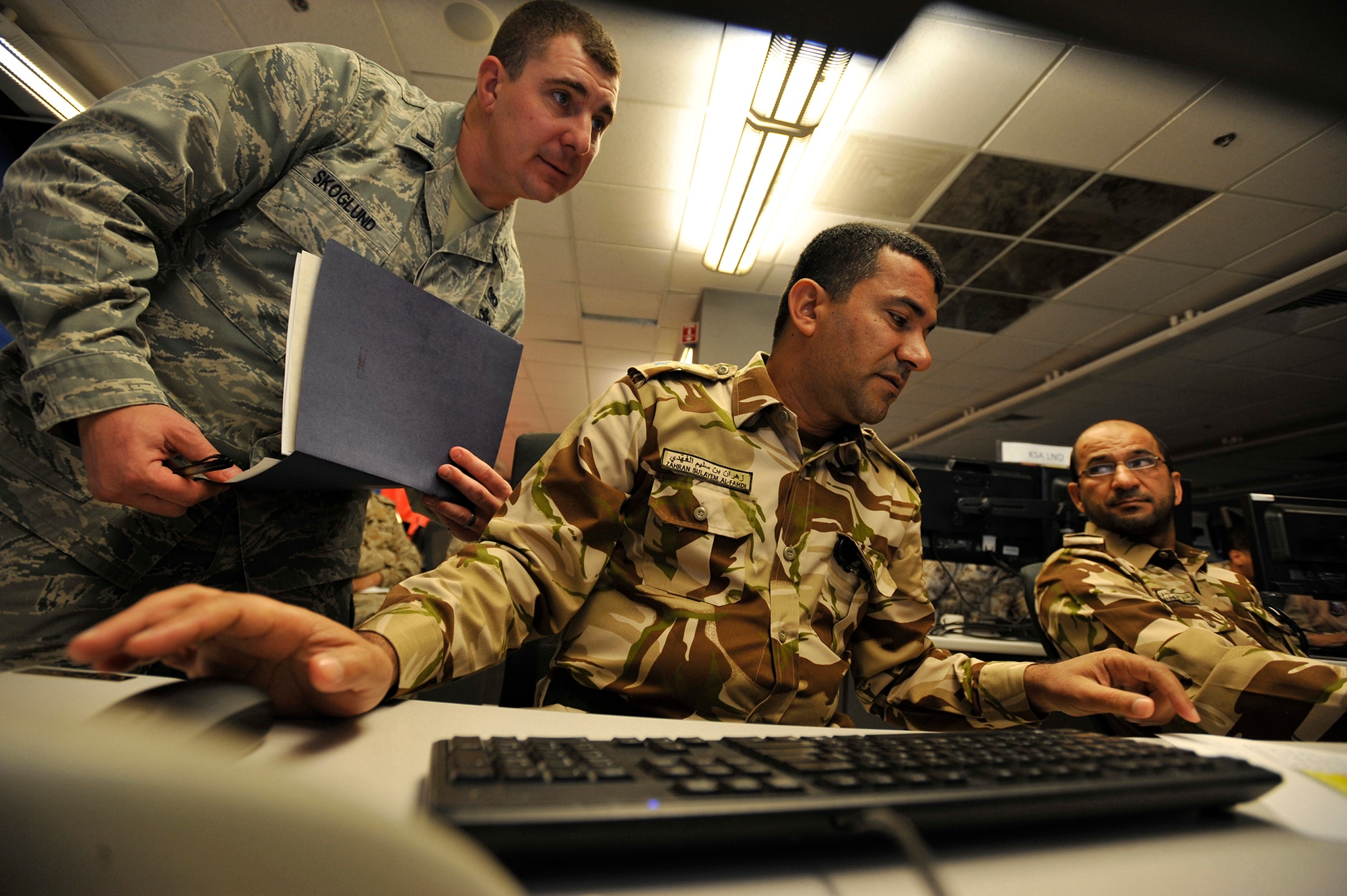 1st Lt. Joshua Skoglund, exercise coordinator, assists Royal Air Force of Oman Wing Commanders Zahran Al-Fahdi and Rashid Al-Shidi during Arabian Gulf Shield, Feb. 3, 2016, in the Combined Air Operations Center, Al Udeid Air Base, Qatar. Arabian Gulf Shield is the culminating exercise for the Gulf Cooperation Council (GCC) Liaison Officer (LNO) Program. The exercise is designed to exercise GCC LNO procedures and connectivity to host nation Air Operations Centers which improves US-GCC interoperability. (U.S. Air Force photo by Master Sgt. Joshua Strang)